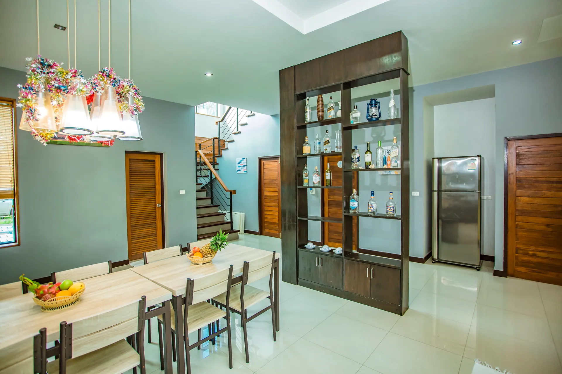 Long dining tables for a large group beside a timber display shelf, with the staircase beyond