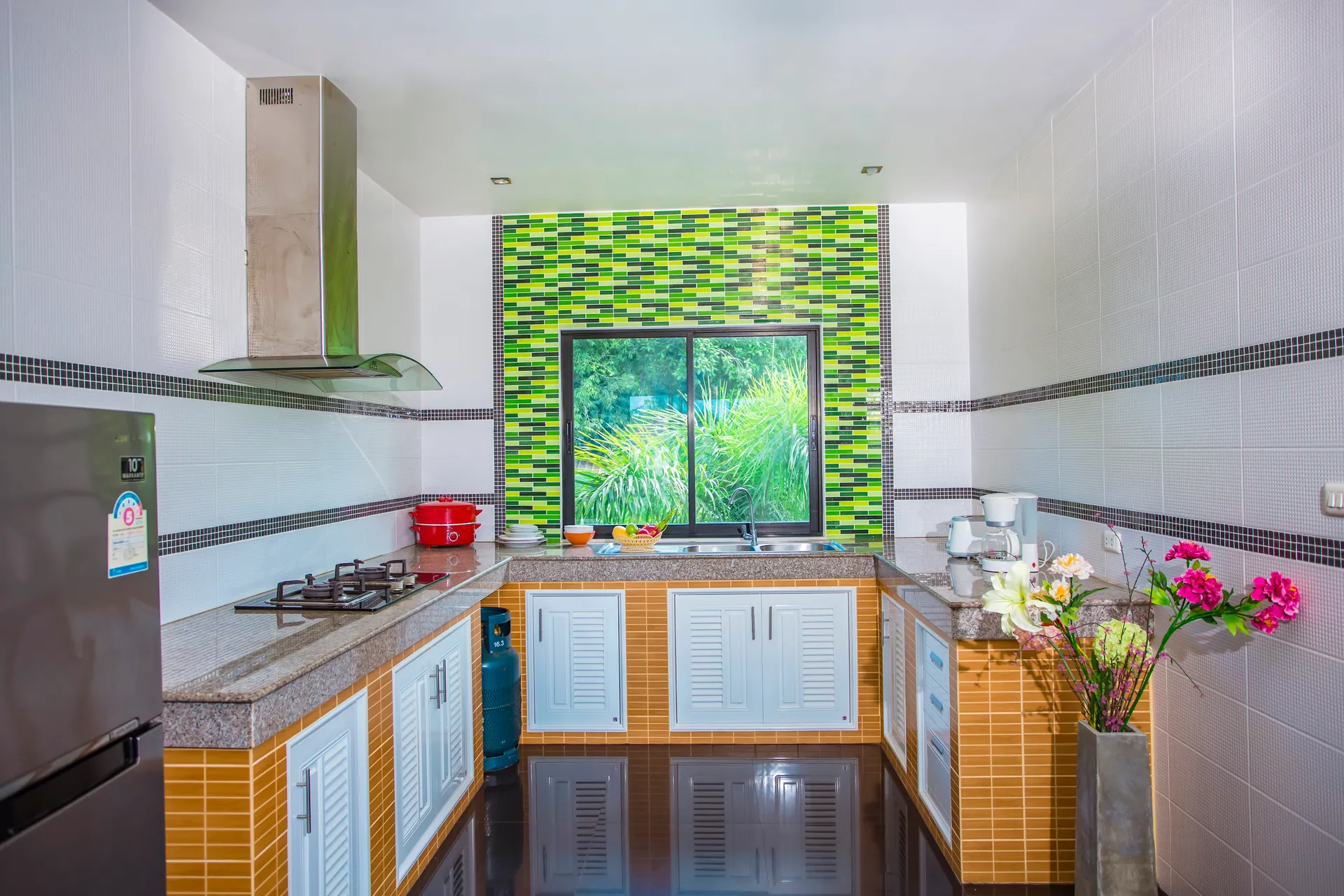 U-shaped kitchen with a gas hob, an extractor hood, a refrigerator and a green mosaic wall around the window