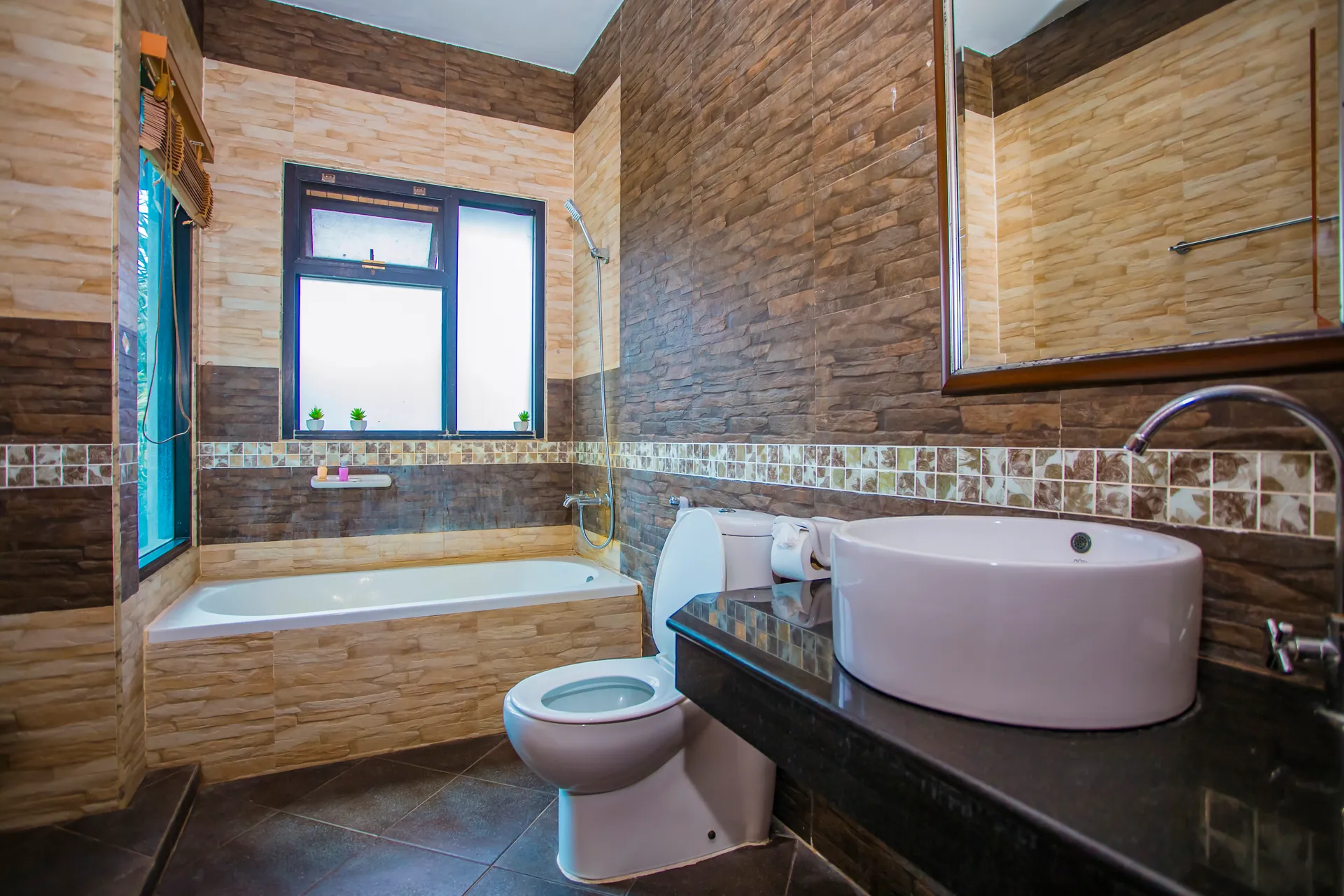 Bathroom with a bathtub, a round vessel basin and stone-effect wall tiles