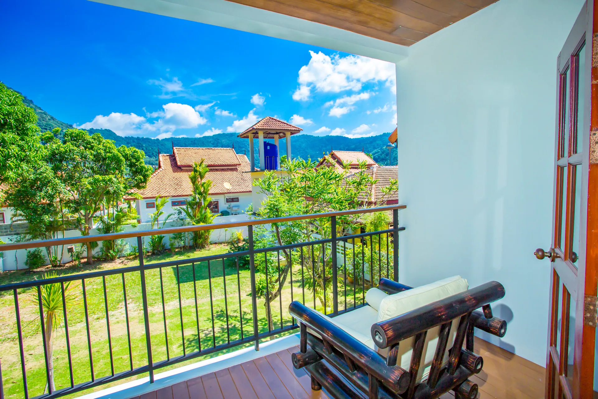 Balcony with a bamboo armchair, looking over the lawn and neighbouring rooftops to wooded hills
