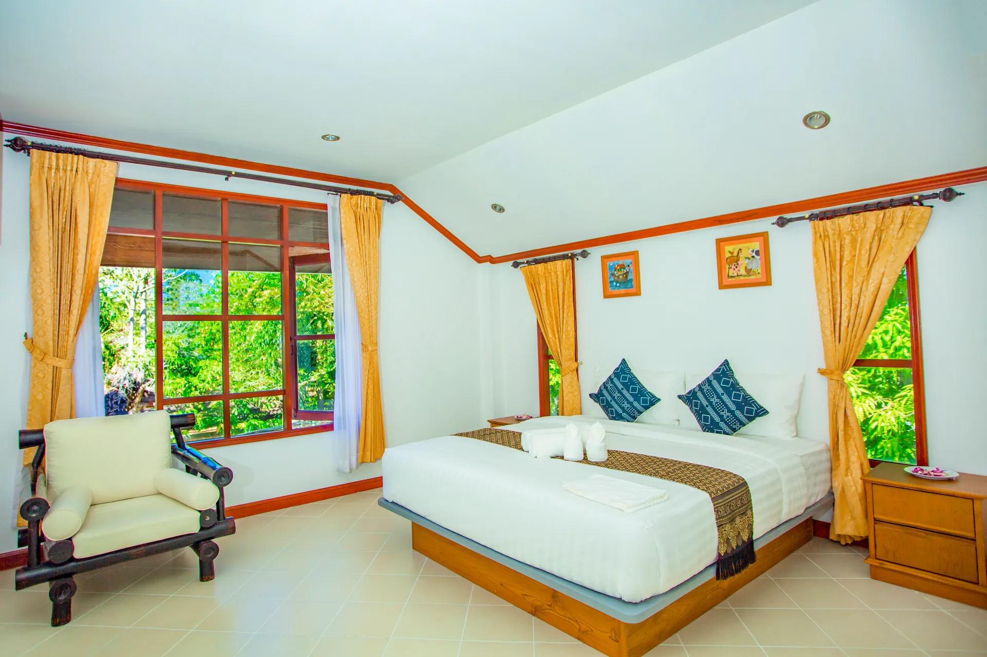 Bedroom with a double bed, an armchair and windows on two sides framed by yellow curtains