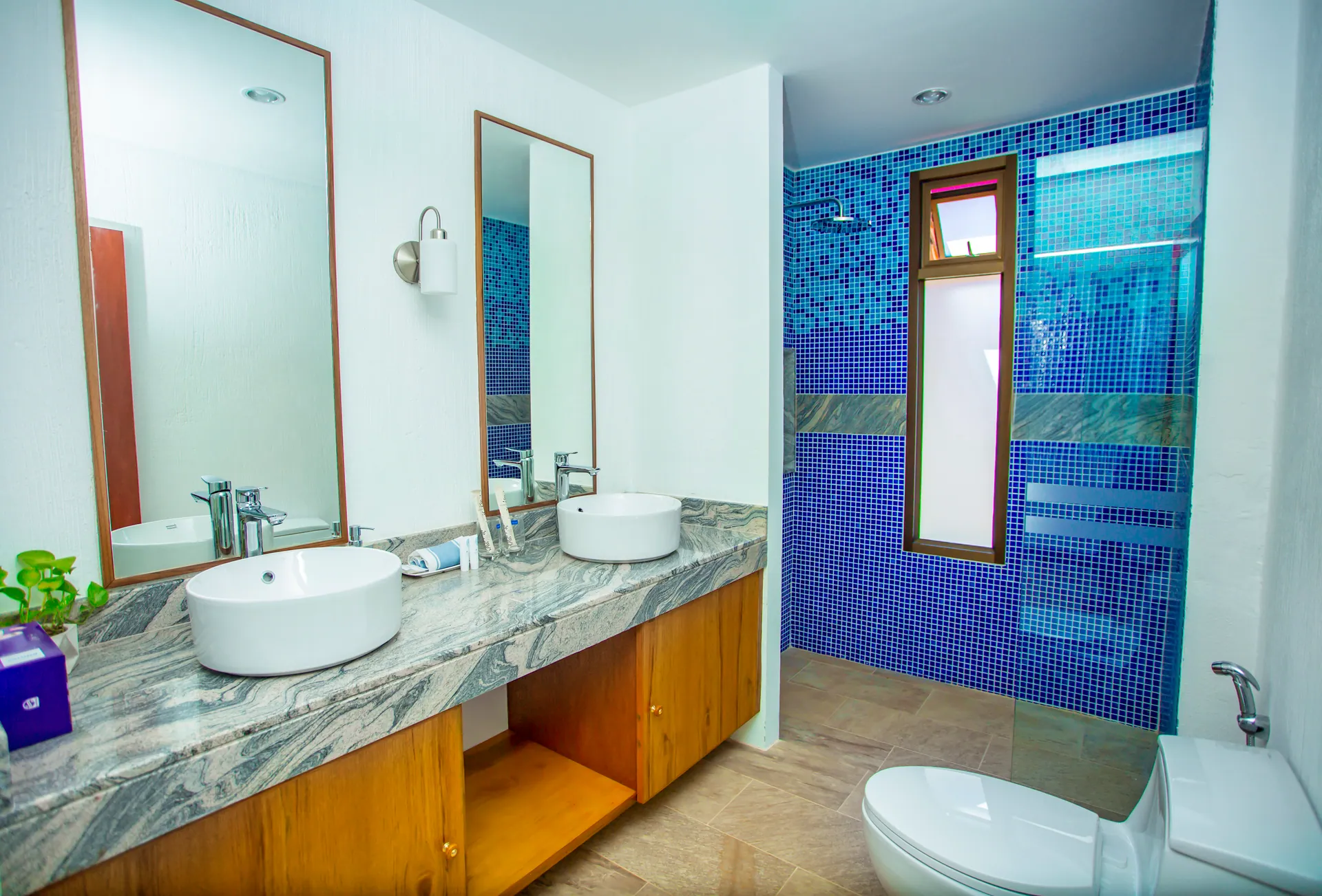 Bathroom with vessel basins on a marble counter and a walk-in shower tiled in blue mosaic