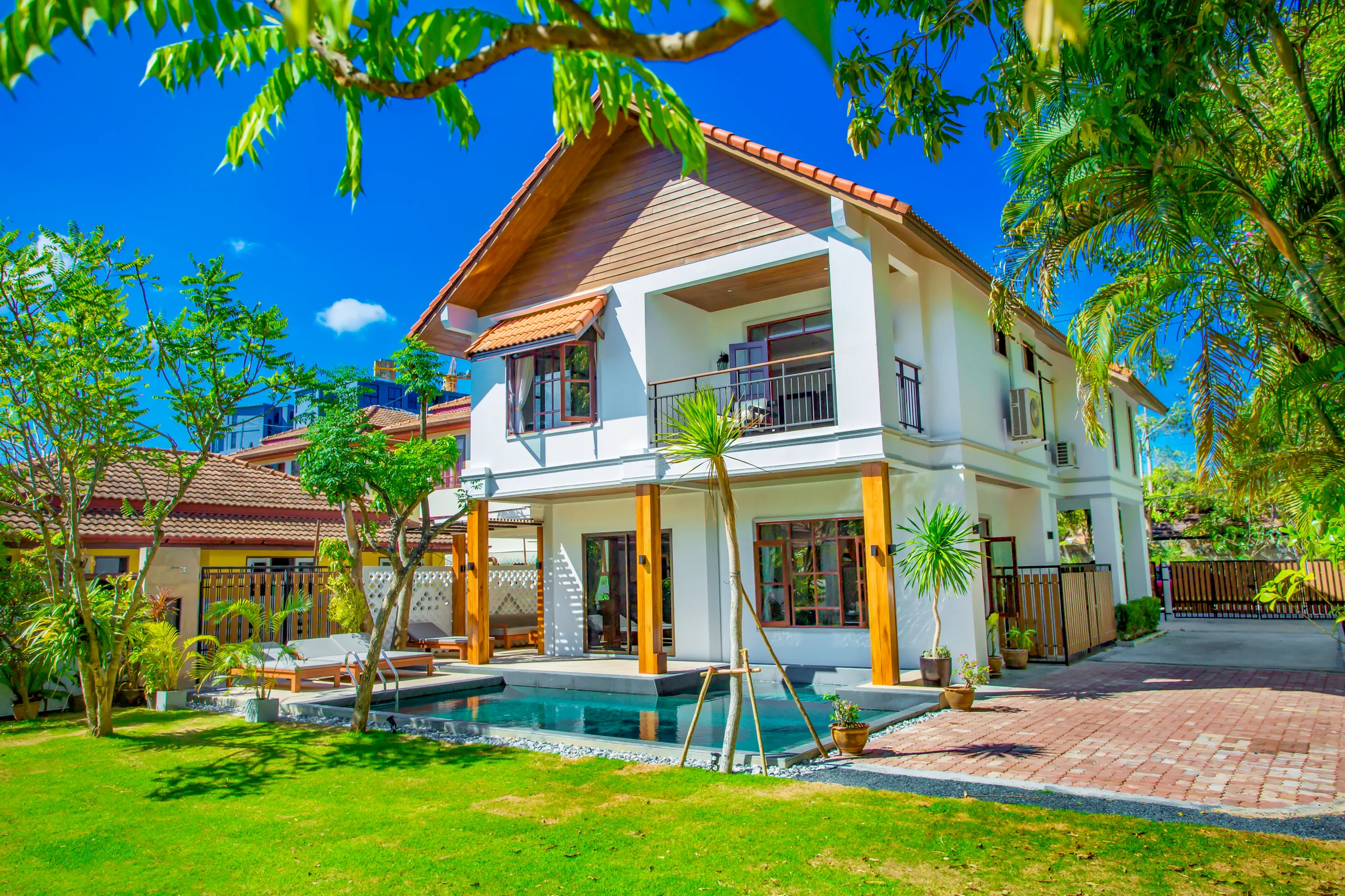 Two-storey white villa with a timber gable, seen across the lawn and private pool through overhanging branches