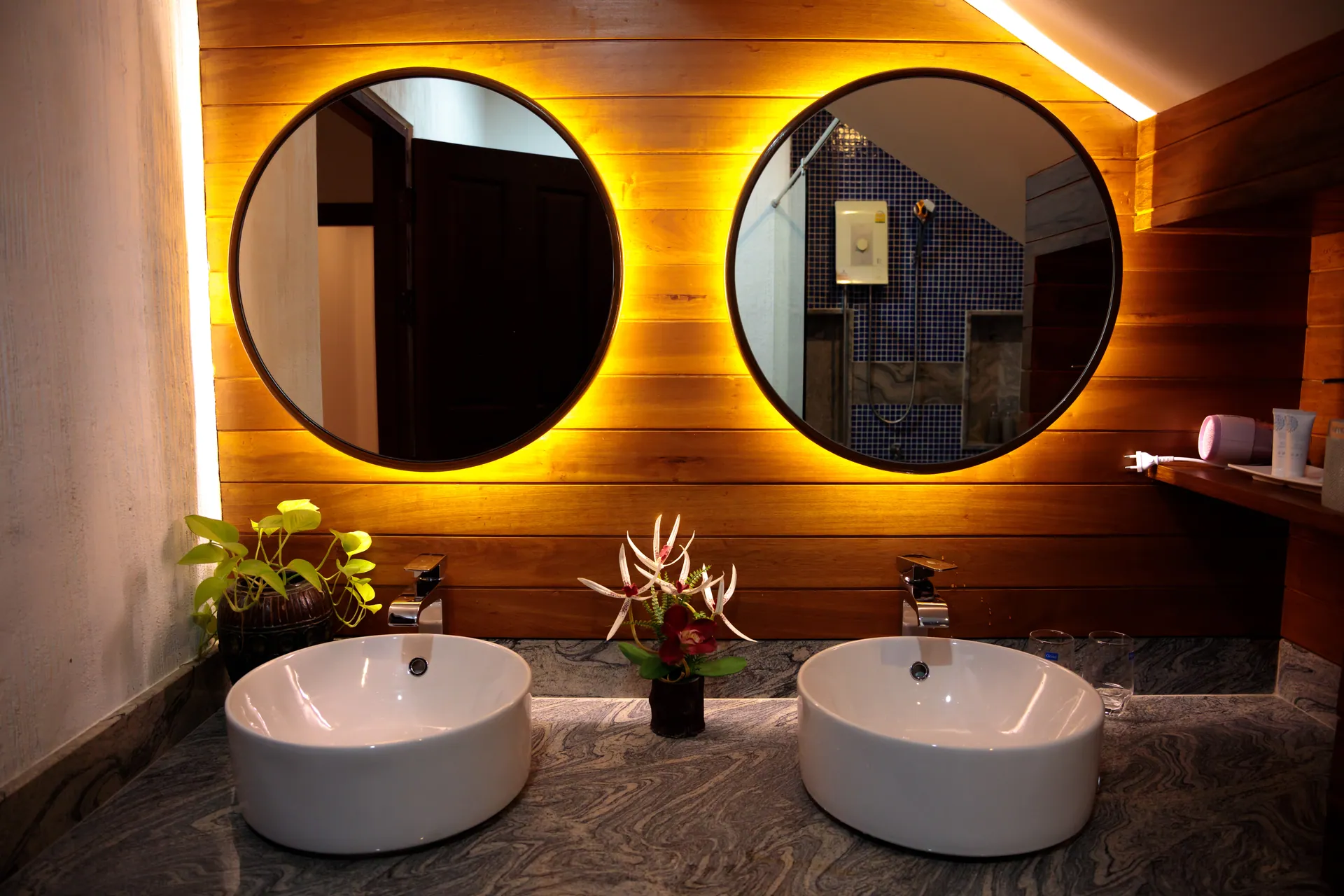 Twin vessel basins below two round backlit mirrors on a timber-panelled wall
