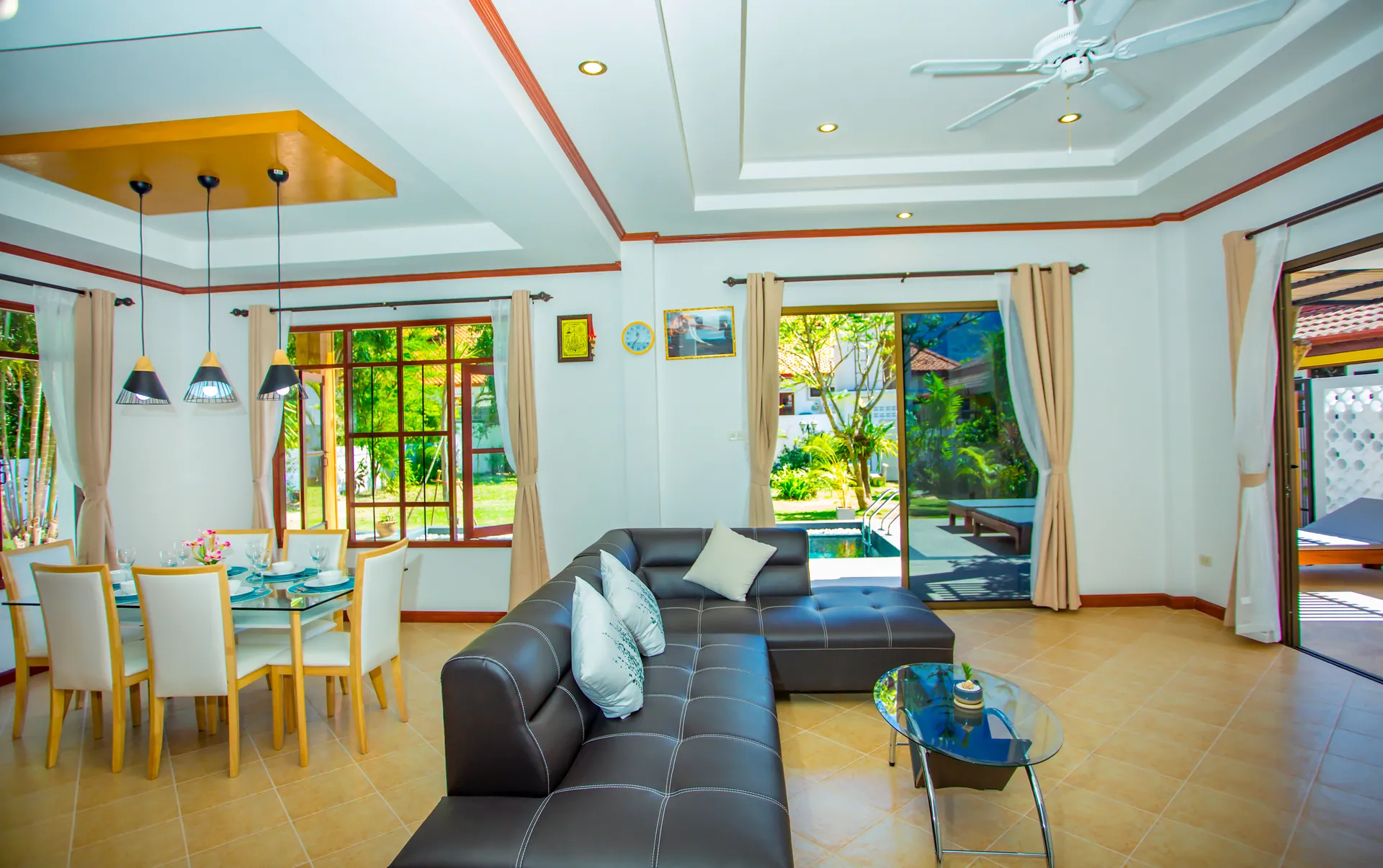 Open-plan living and dining room with a leather corner sofa, pendant lights and glass doors to the pool