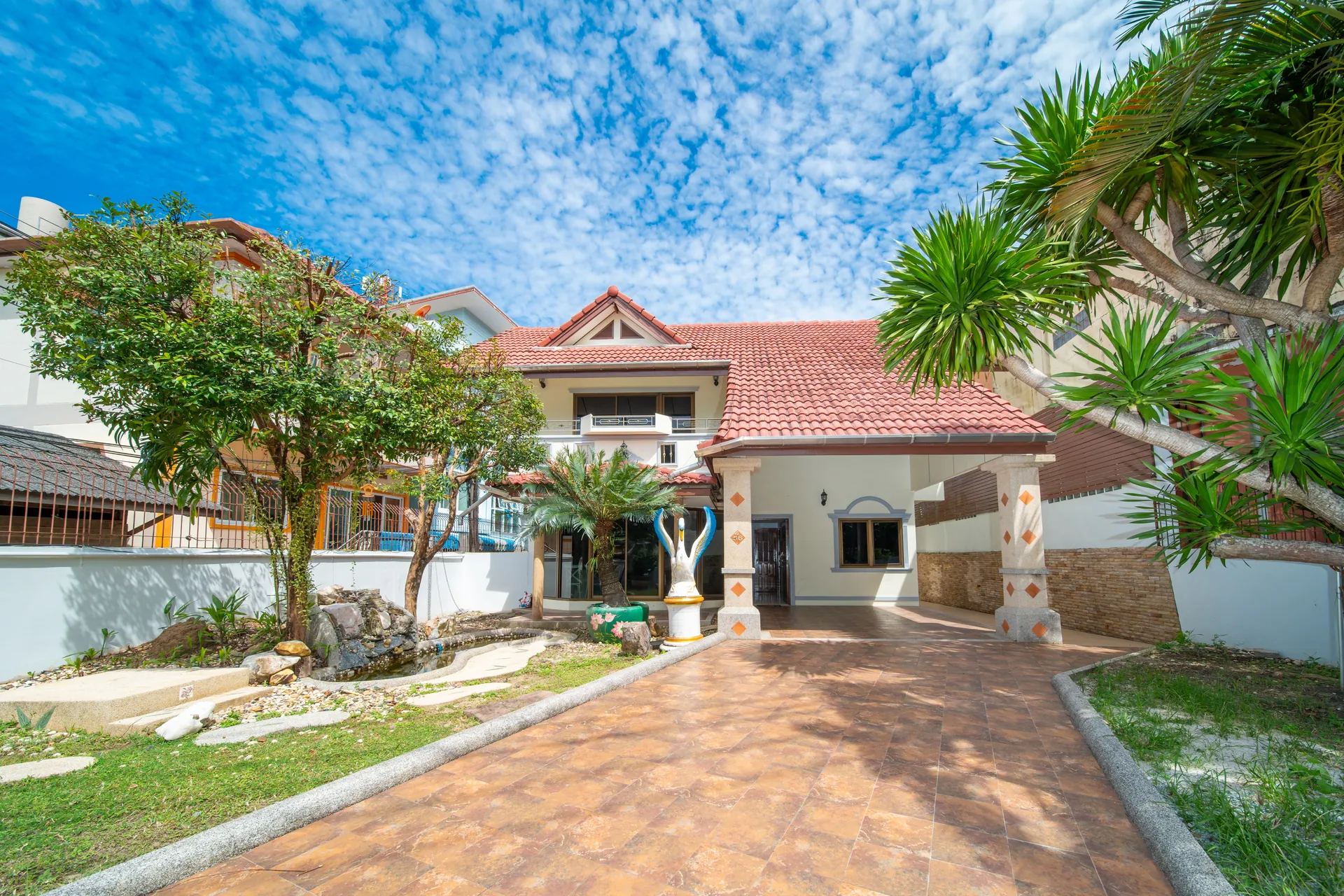 Tiled driveway leading to the front of the two-storey house, with a red tiled roof and palms