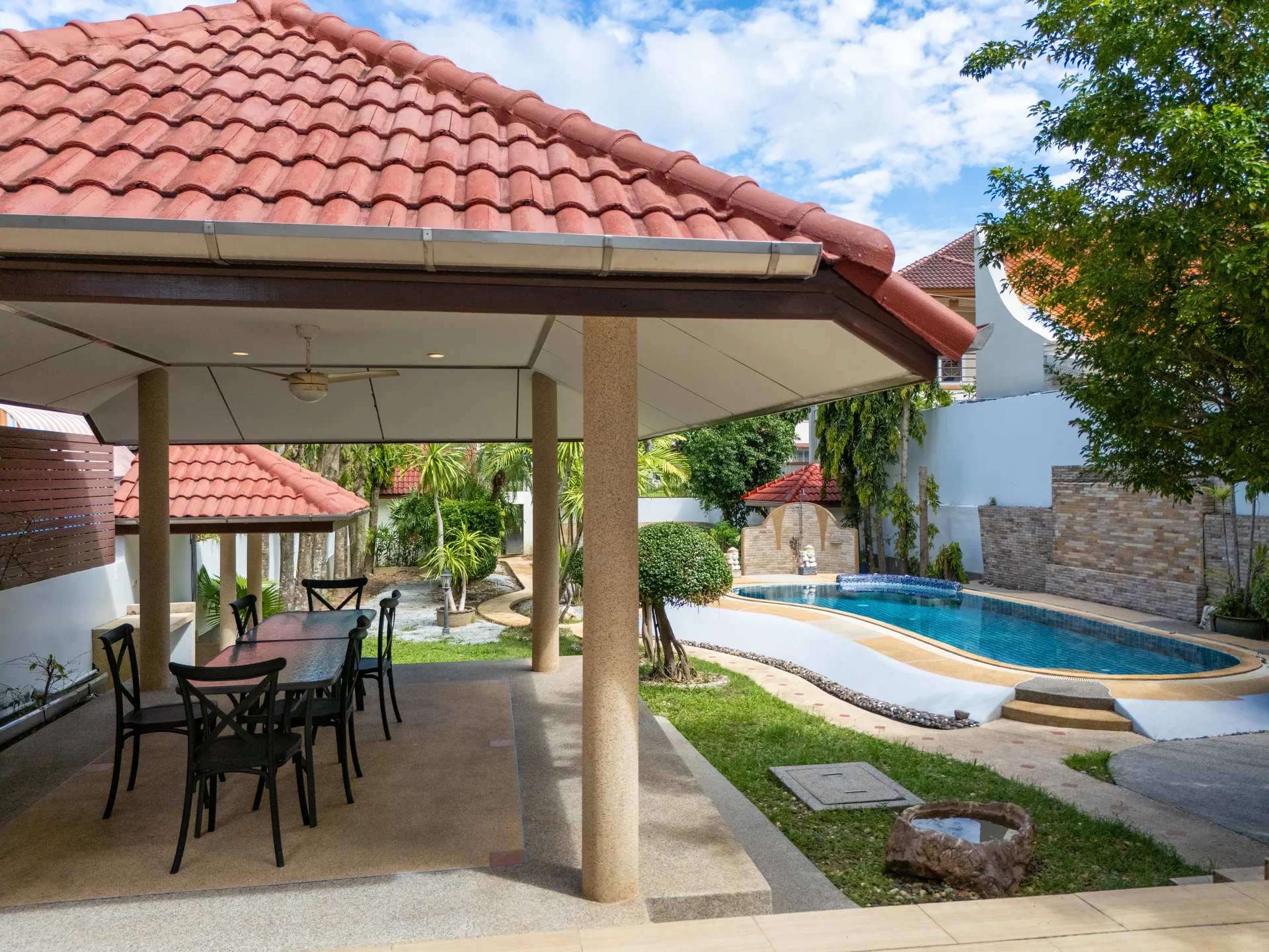 Tiled-roof sala with an outdoor dining table, looking across the lawn to the pool