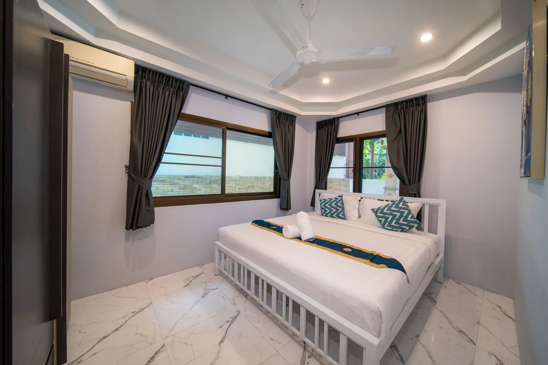 Bedroom with a large white-framed bed, a marble-effect floor and windows on two walls