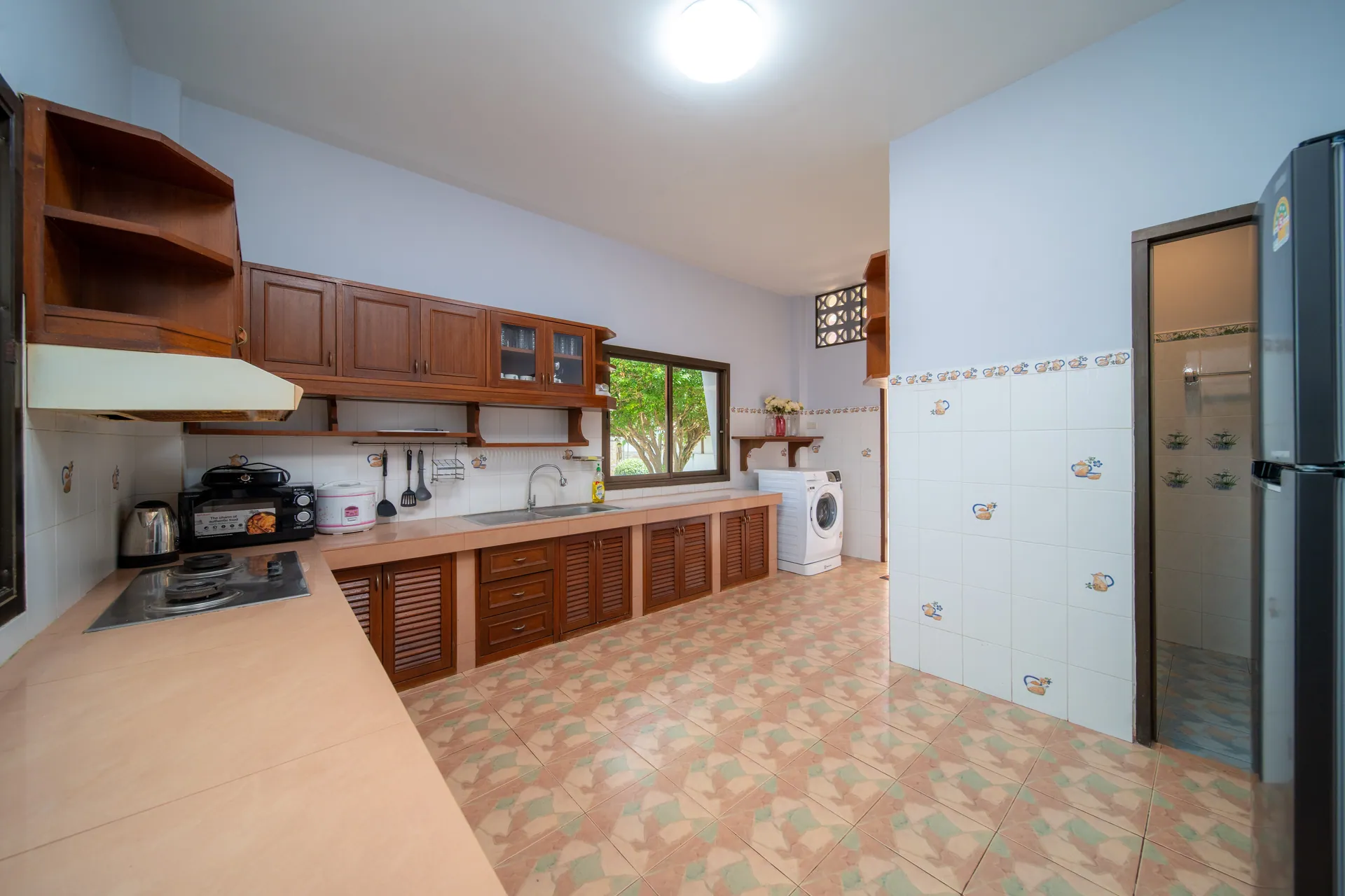 Kitchen with timber cabinets, a gas hob, a double sink, a washing machine and a tall fridge