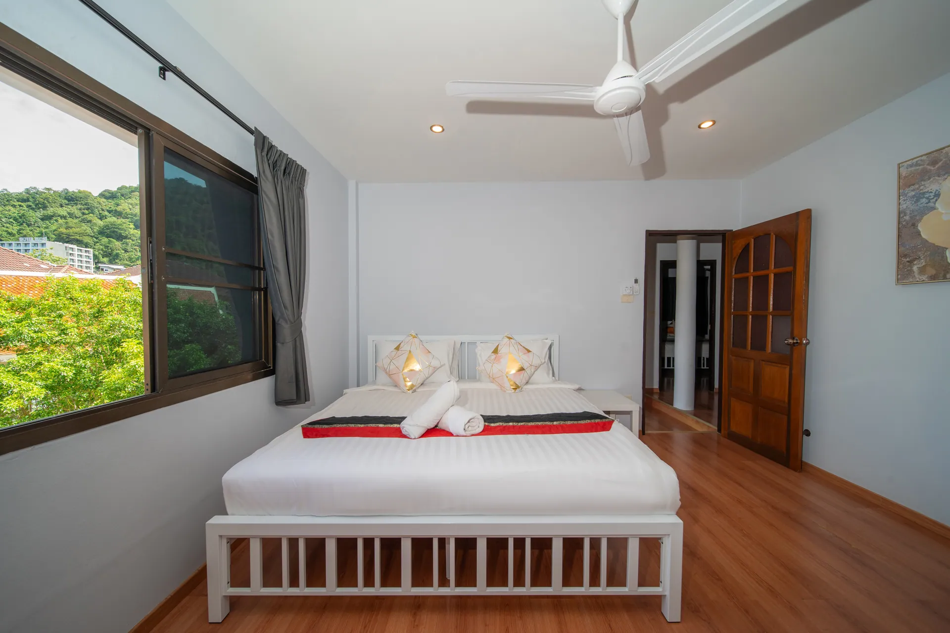 Bedroom with a timber-effect floor, a ceiling fan and a window onto green hills