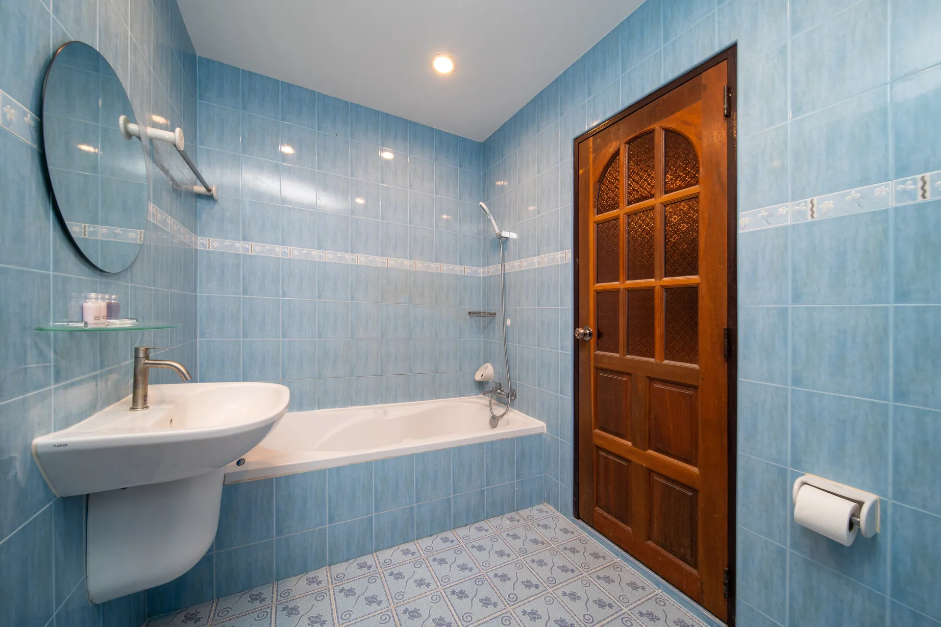 Blue-tiled bathroom with a bathtub, a hand shower and a carved timber door