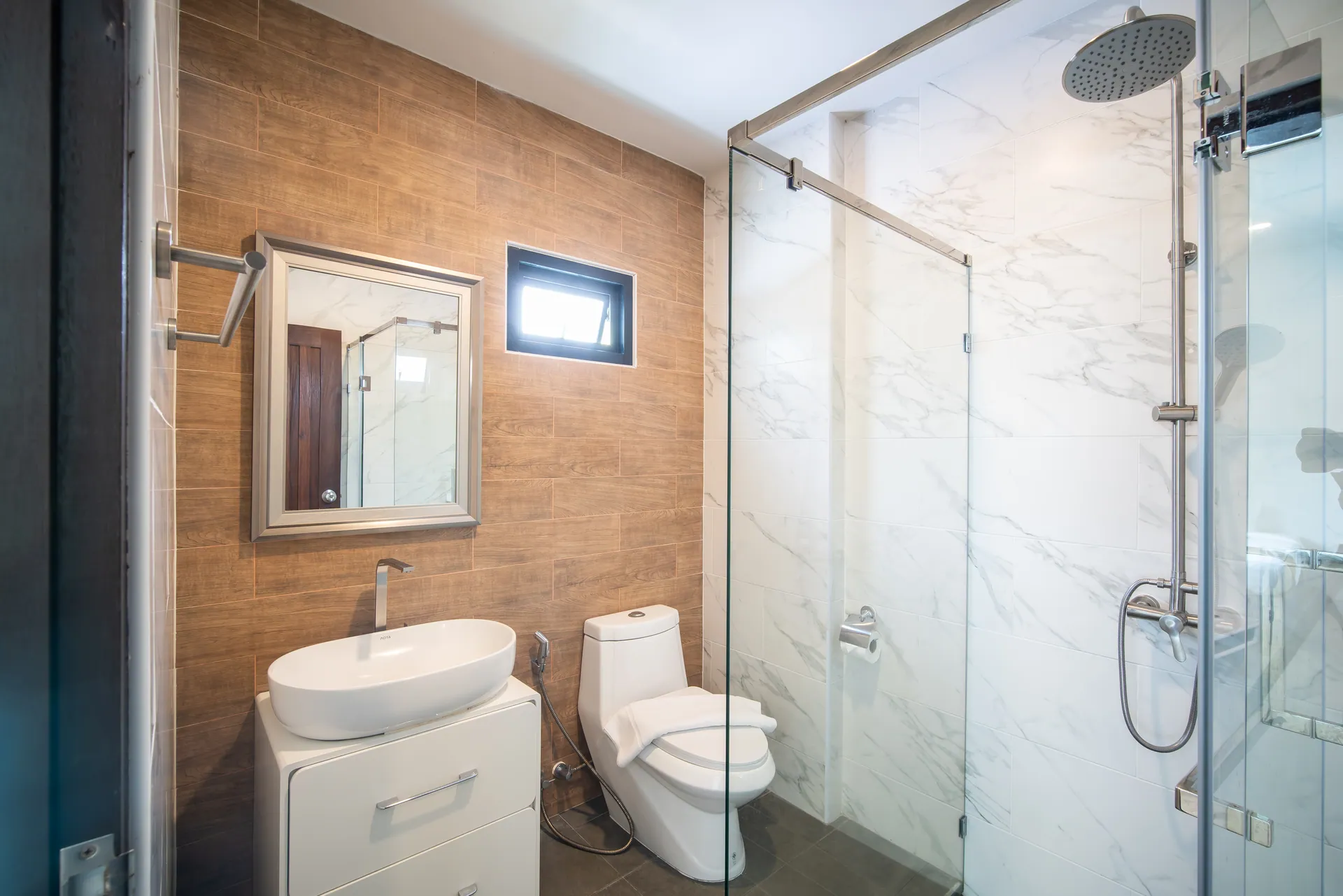 Bathroom with a vessel basin on a white cabinet, a timber-effect feature wall and a glass-enclosed shower