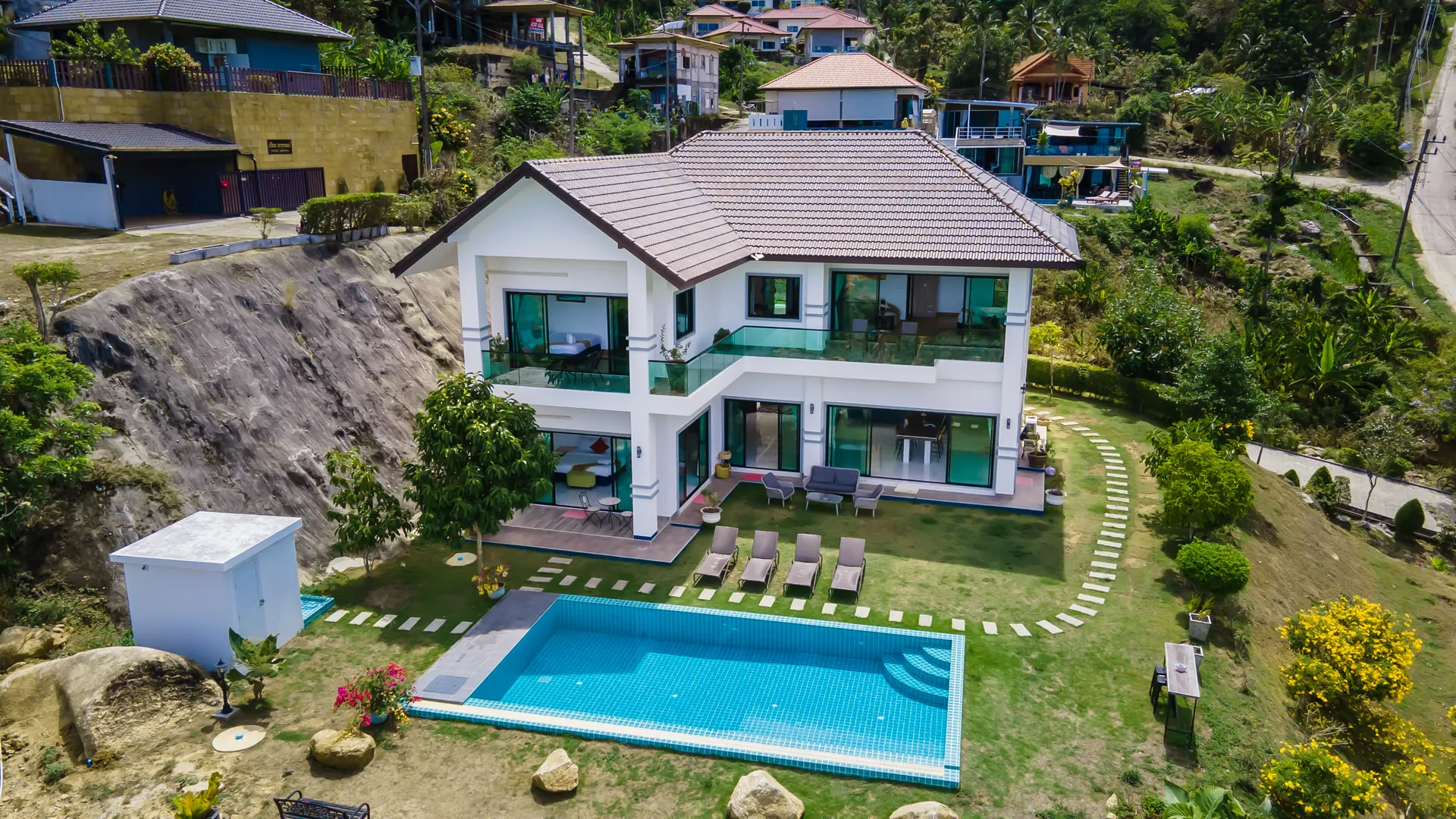 Aerial view of the two-storey white villa on its hillside plot, with the private pool and lawn in front