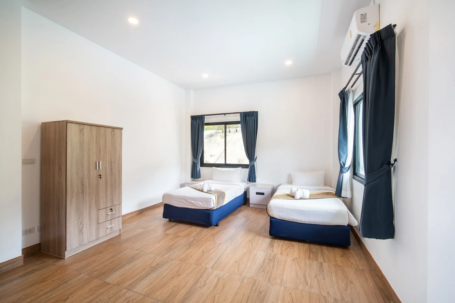 Twin bedroom with two single beds, a timber wardrobe and windows on two sides