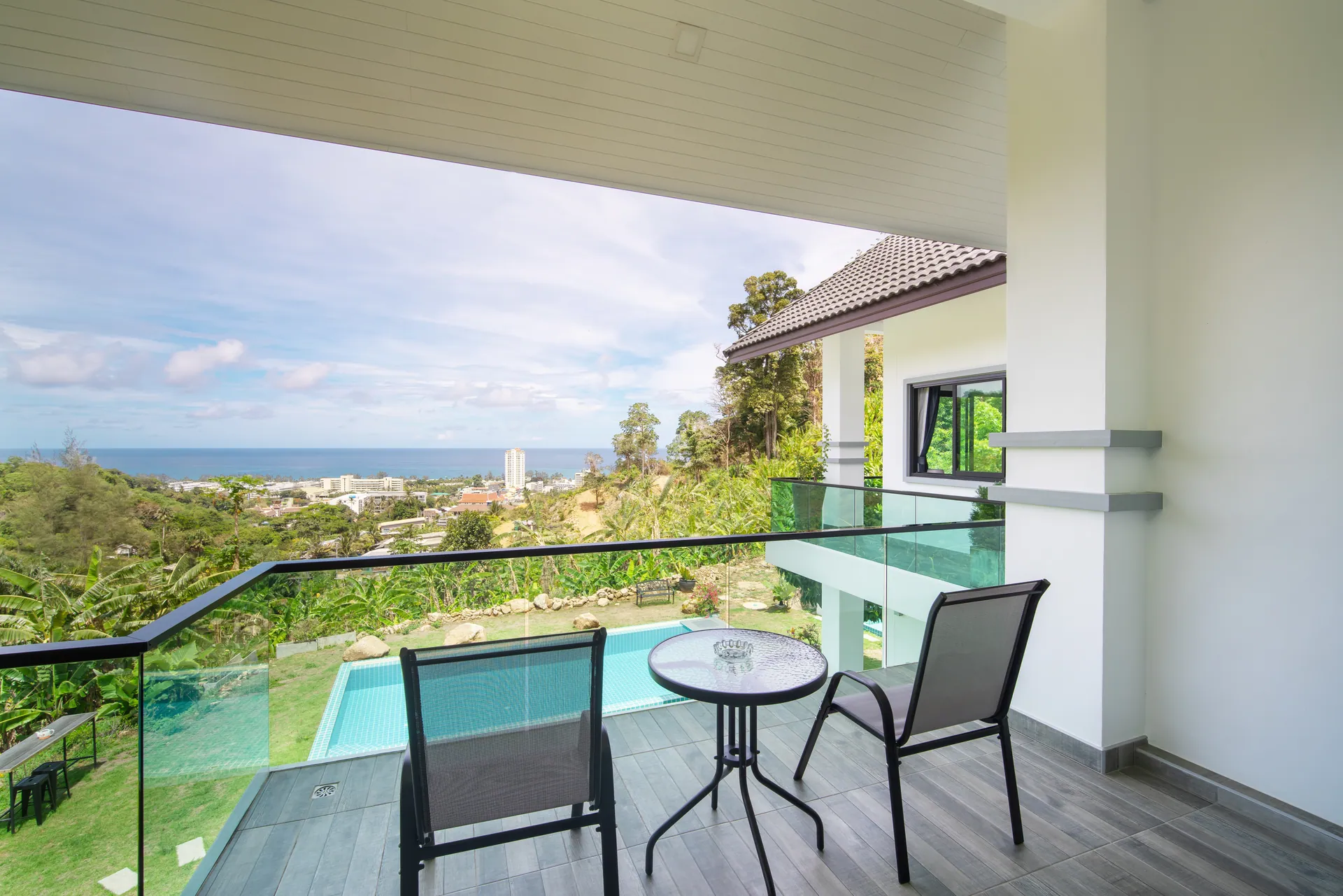 Upper-floor terrace with a bistro table and glass balustrade, looking over the pool and down the valley to the sea