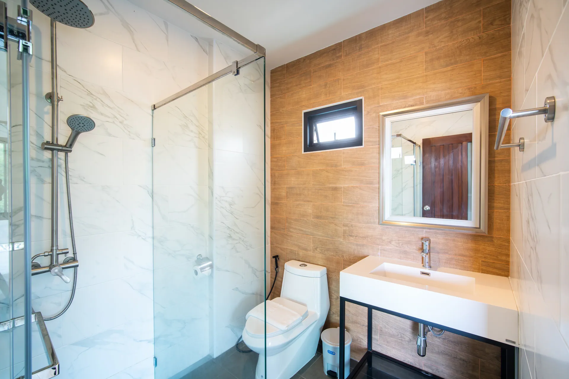 Bathroom with marble-effect walls, a timber-effect feature wall and a glass-enclosed rain shower