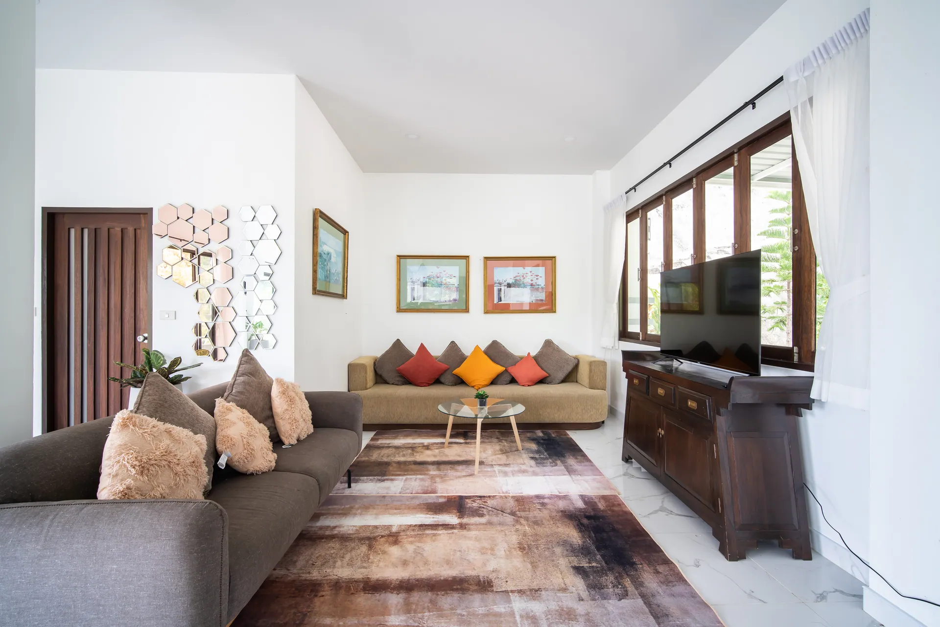 Living room with two sofas, a patterned rug and a television on a carved timber cabinet