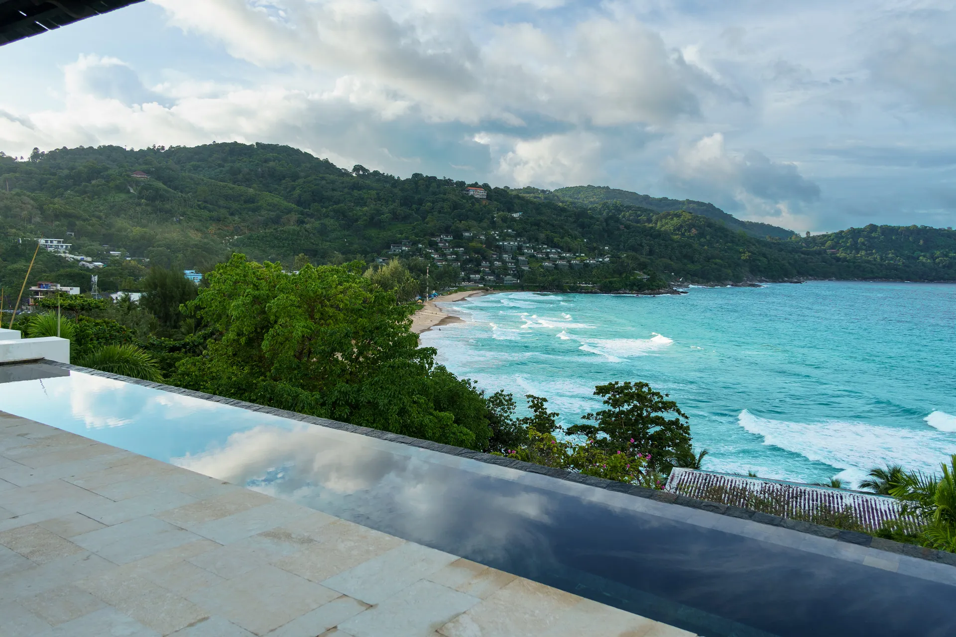 The pool's infinity edge, looking down over the treetops to a curving beach and wooded hills