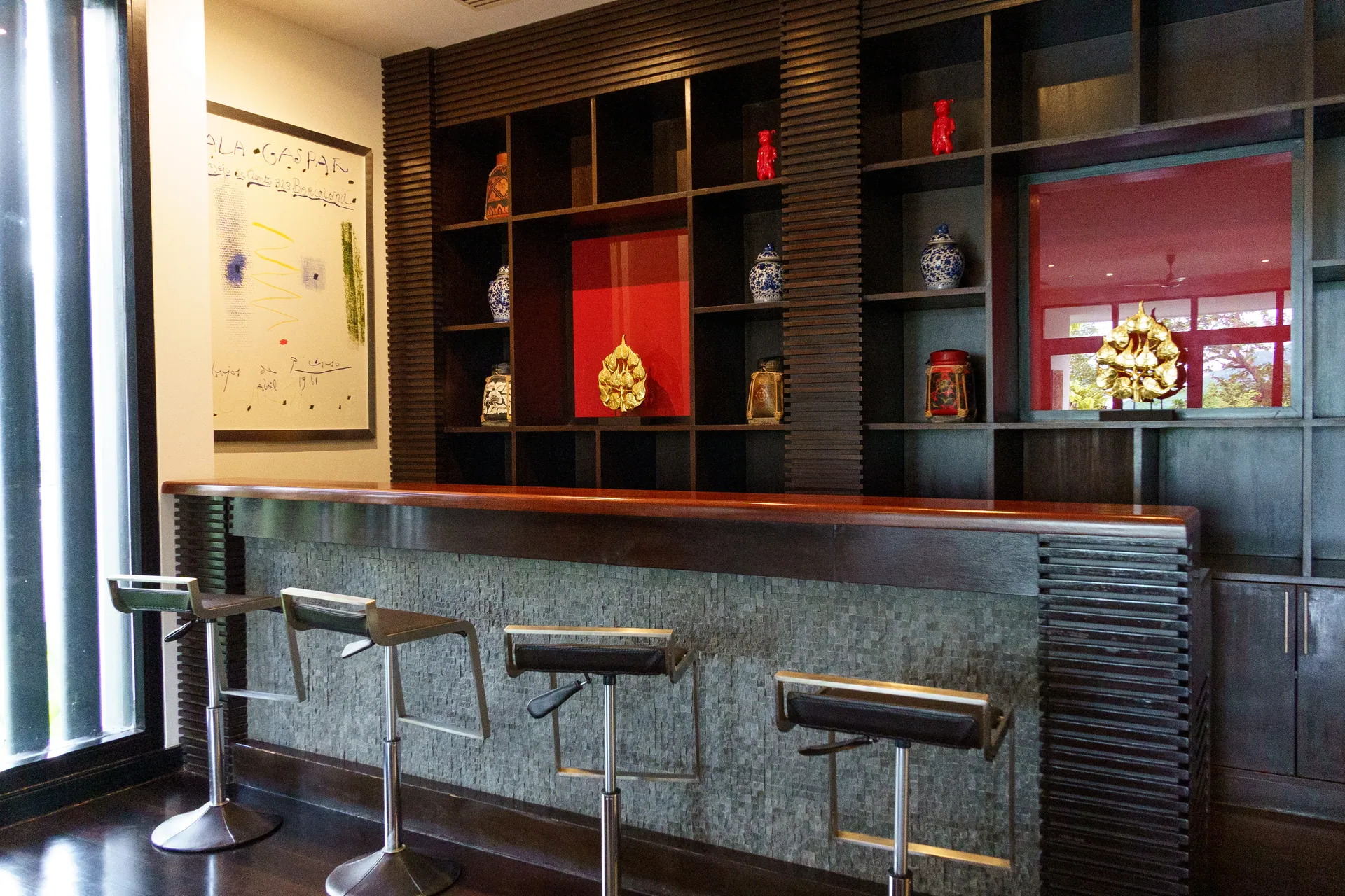 Bar counter with four stools, set against dark timber shelving with red lacquered niches