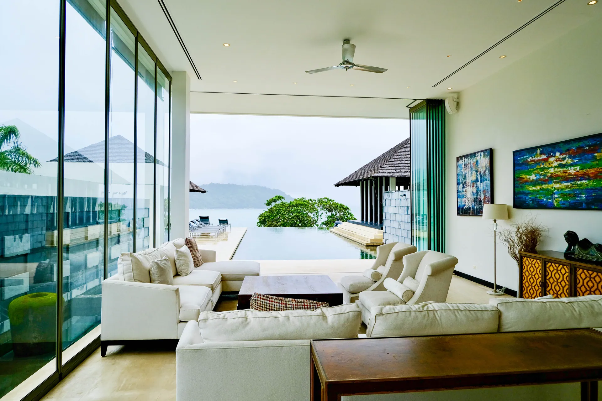 Living room with glass walls and sofas, open to the pool terrace and the sea