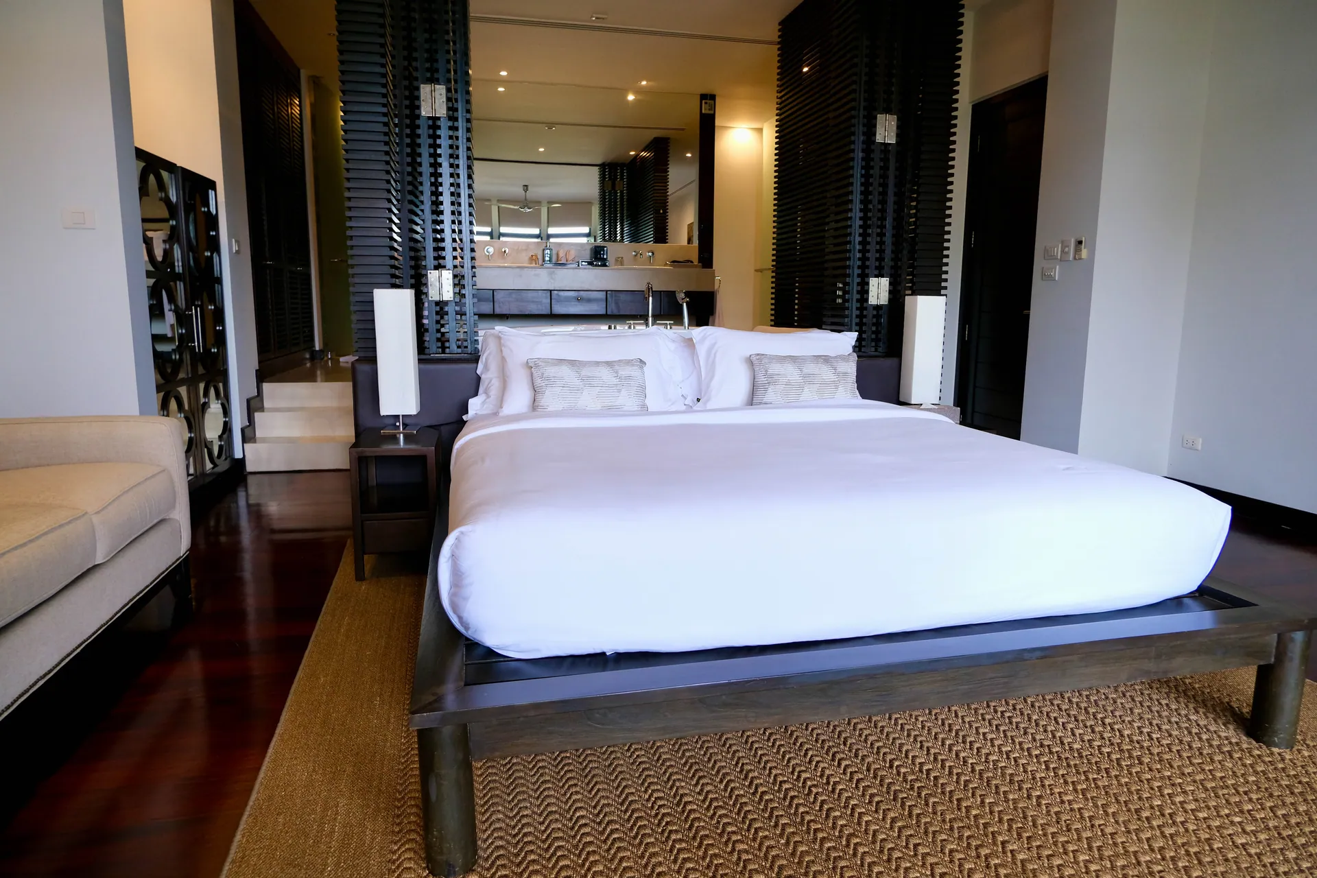 Bedroom with a low timber bed on a sisal rug, and slatted screens leading to the bathroom