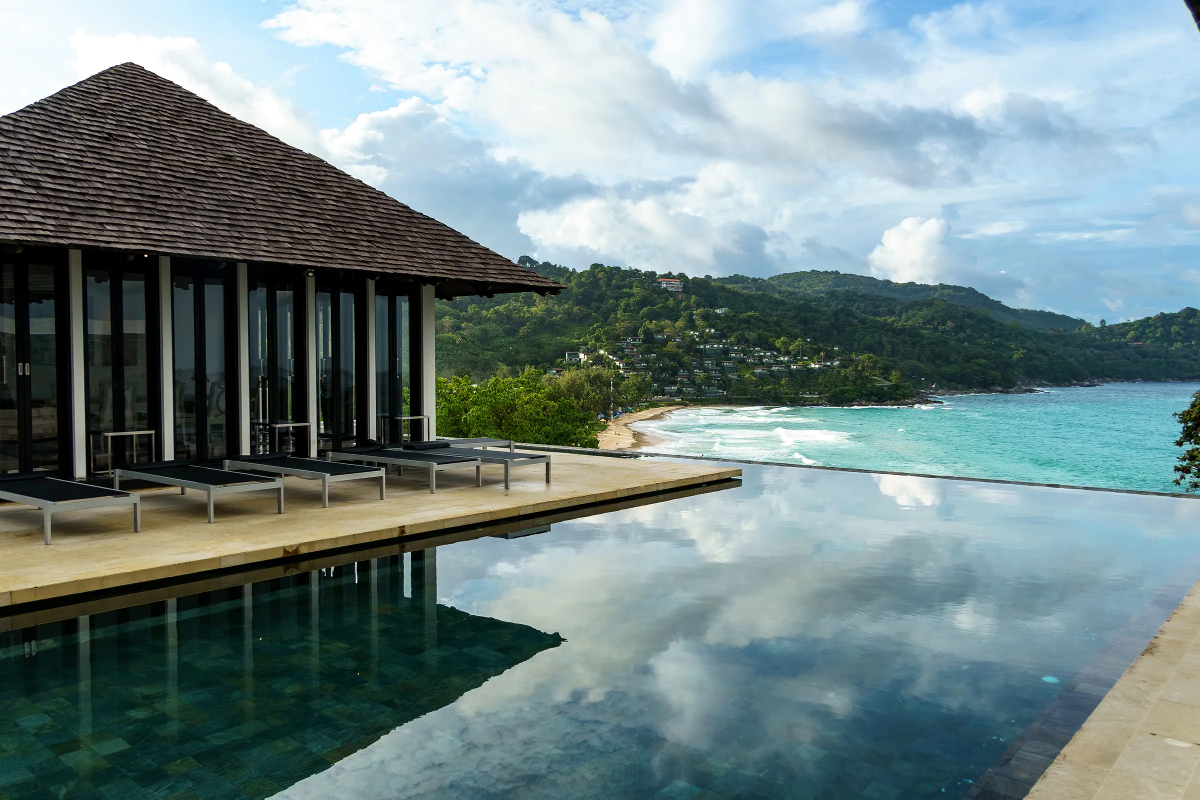 Infinity pool beside a pavilion with a pyramid roof, overlooking a bay and its beach