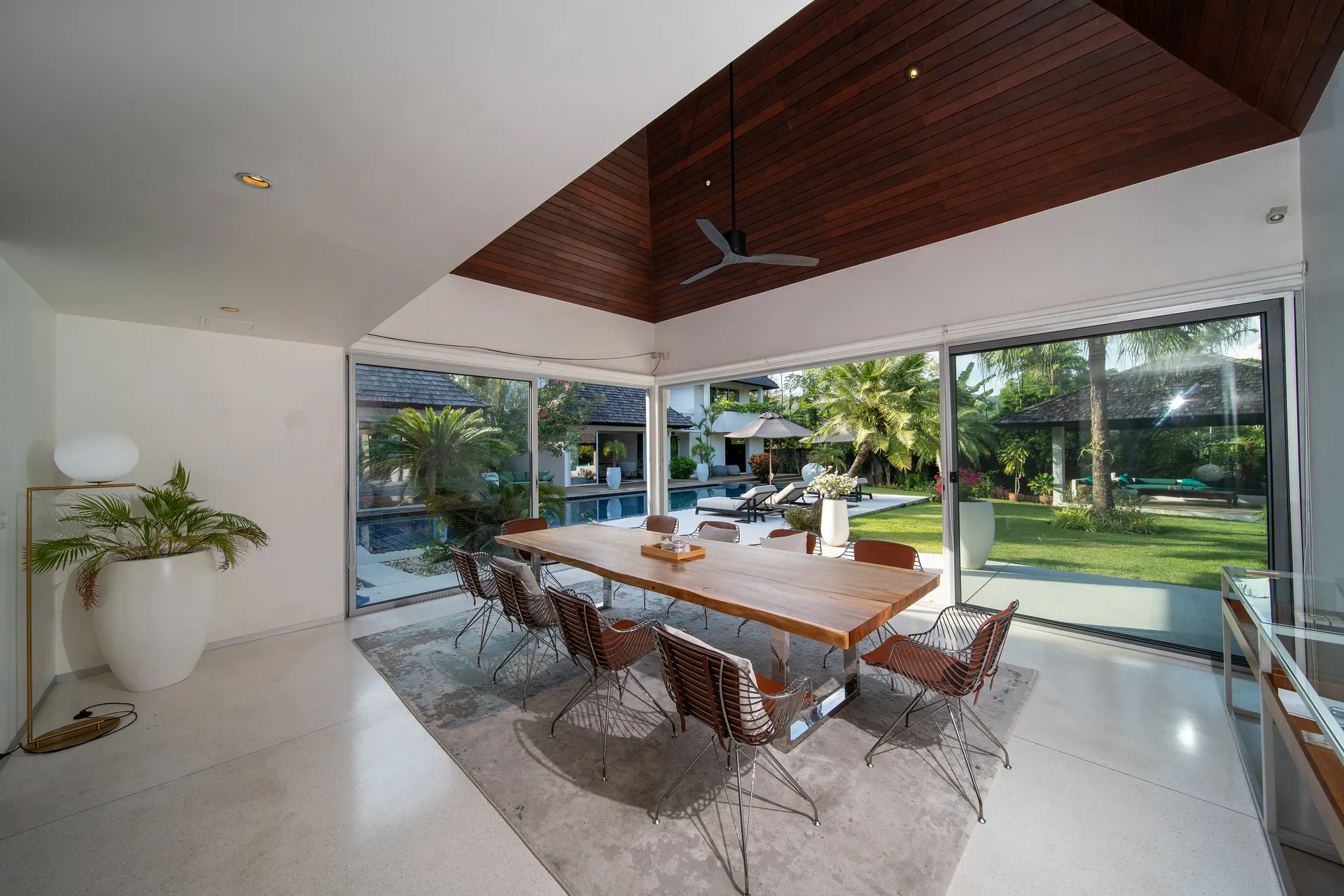 Long timber dining table beside sliding glass doors, with the pool and garden beyond