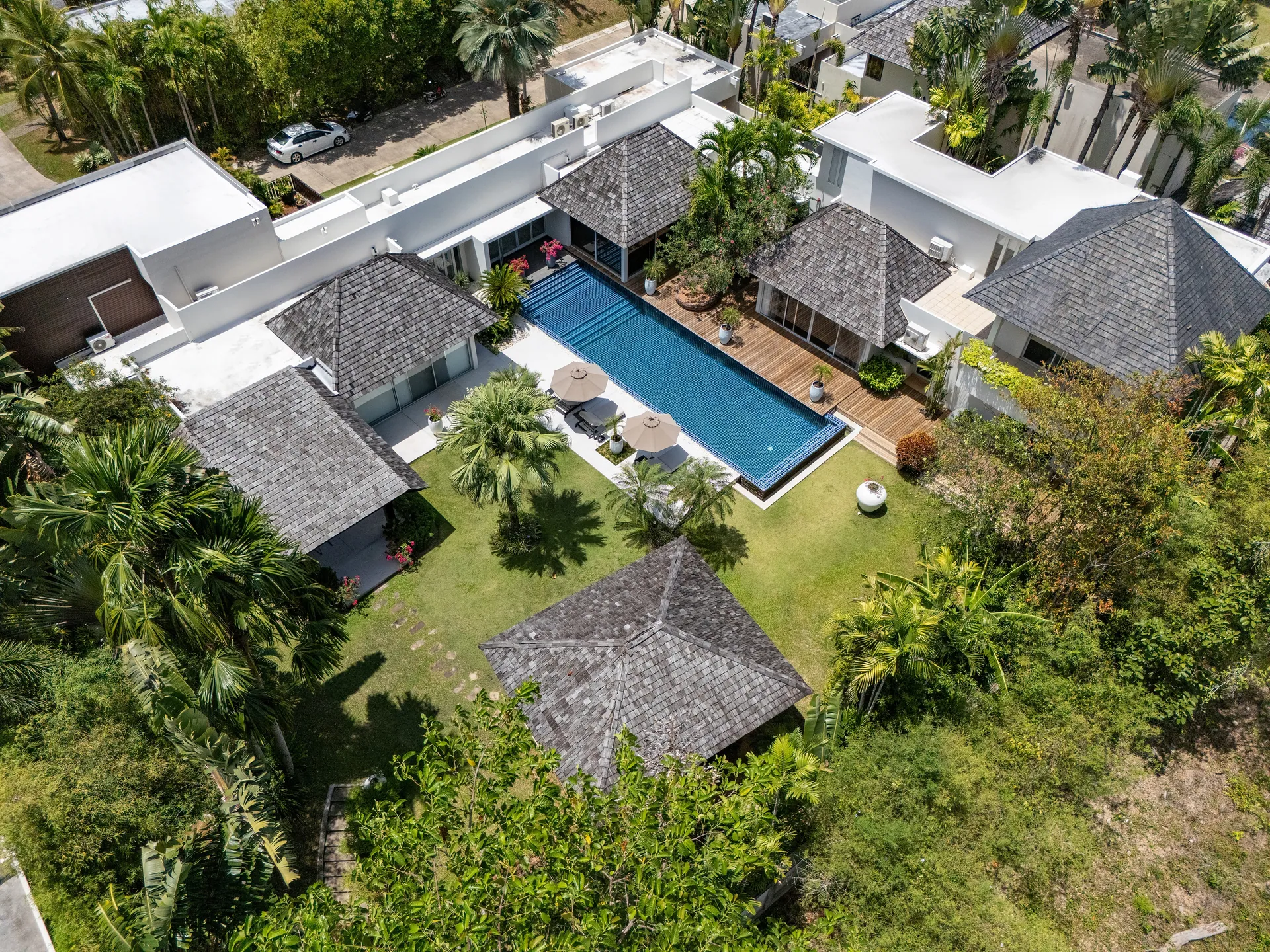 Aerial view of the villa: shingle-roofed pavilions around a long pool and a lawn, framed by tropical trees