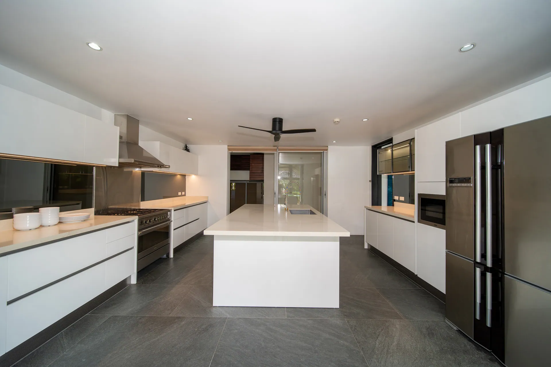 White kitchen with a central island, a stainless steel cooker hood and a tall double-door fridge