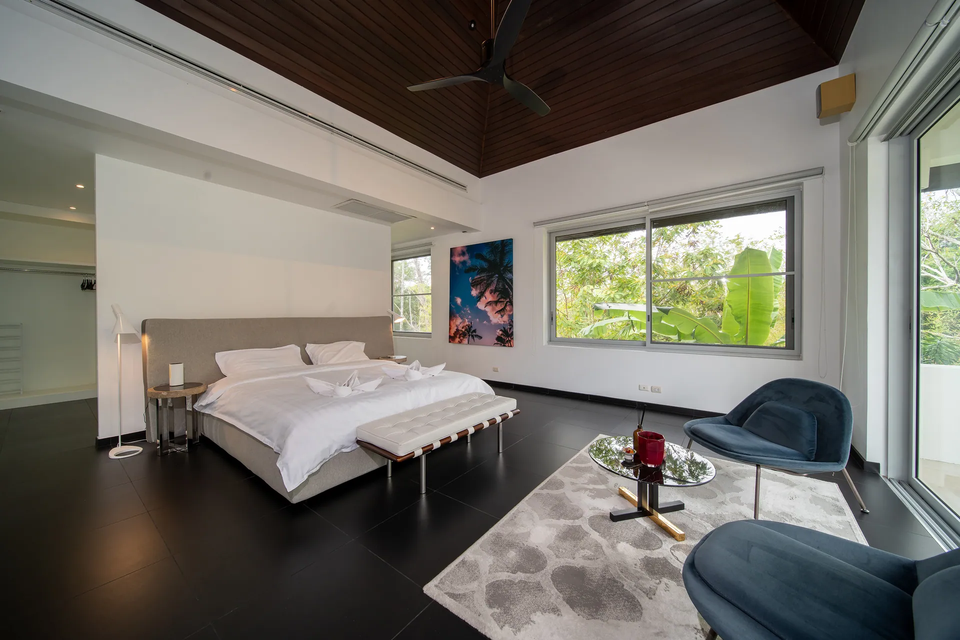 Bedroom under a vaulted timber ceiling, with a bench at the foot of the bed and two blue armchairs