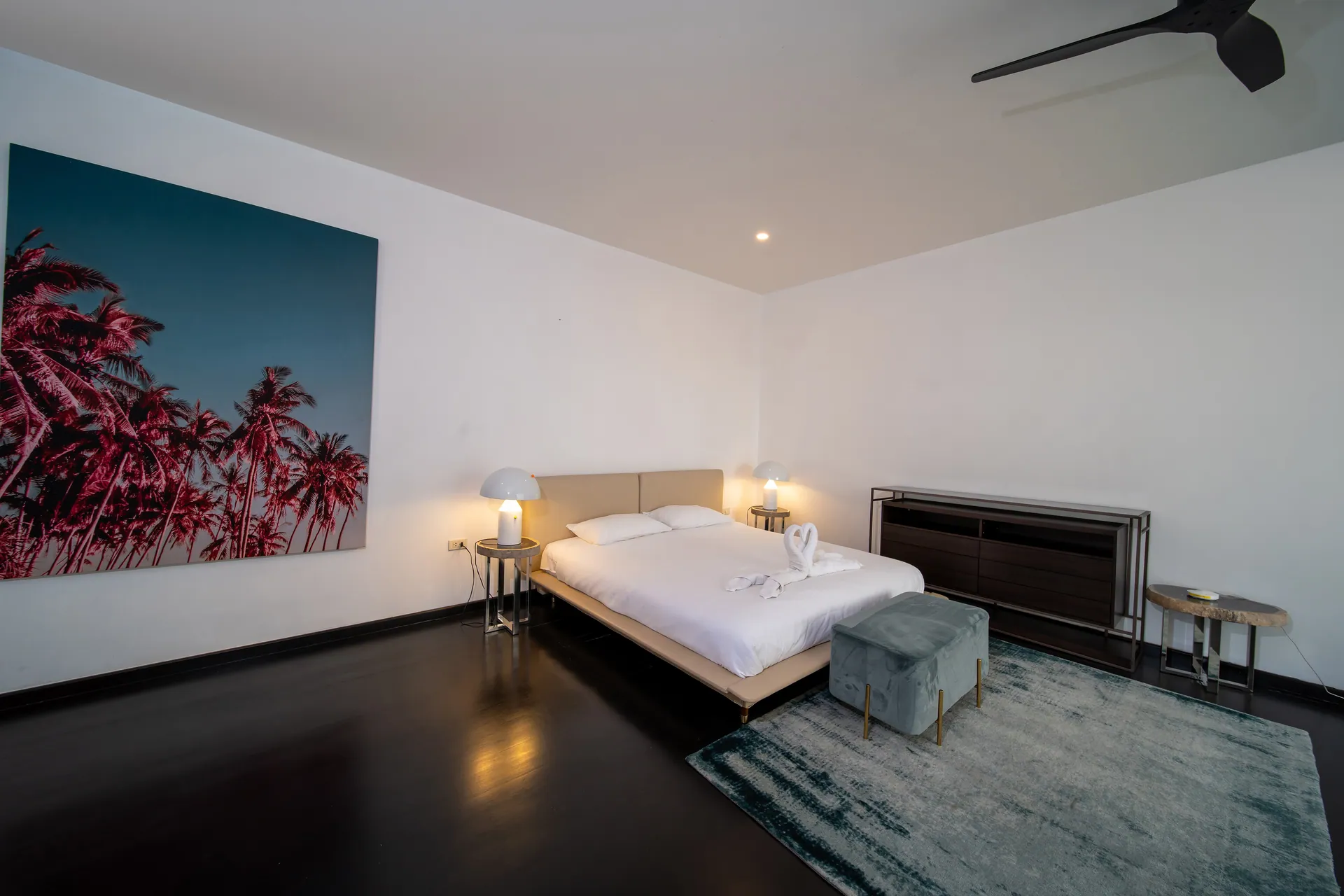 Bedroom with a low bed, a dark wood sideboard and a large photograph of palms against a blue sky