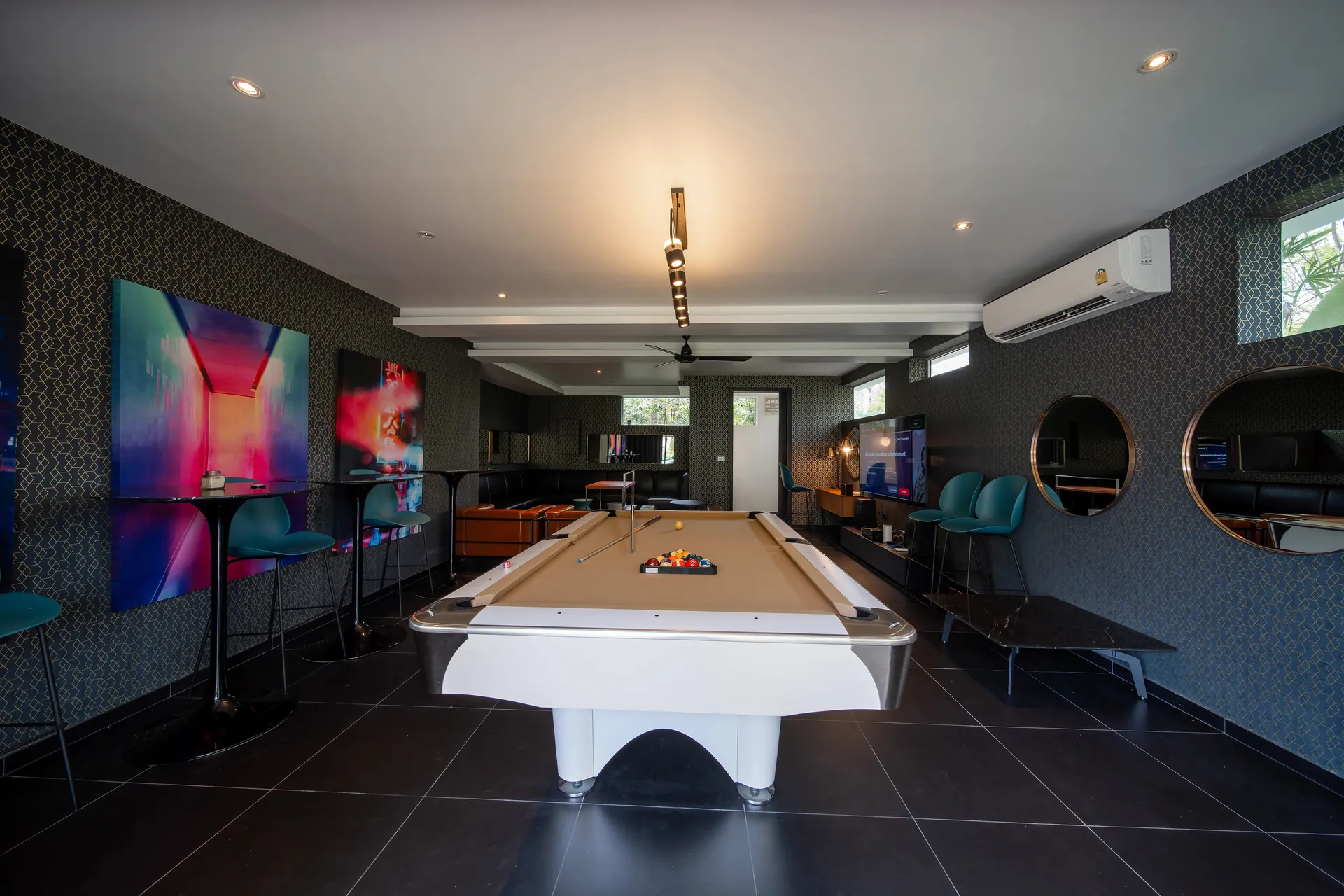 Games room with a pool table, bar stools along a counter and colourful artworks on the walls