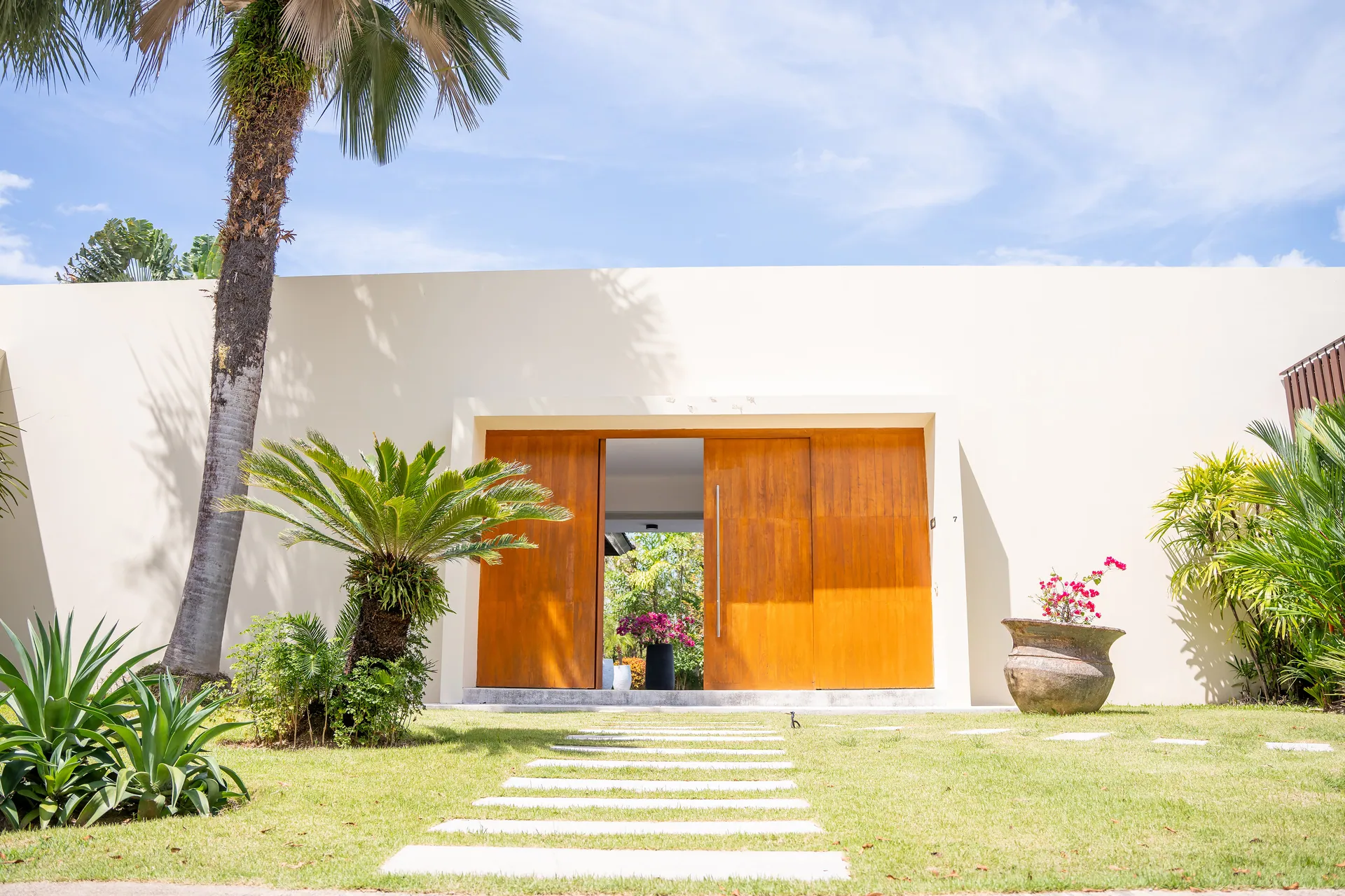 Tall timber entrance doors set in a white garden wall, reached by stepping stones across the lawn
