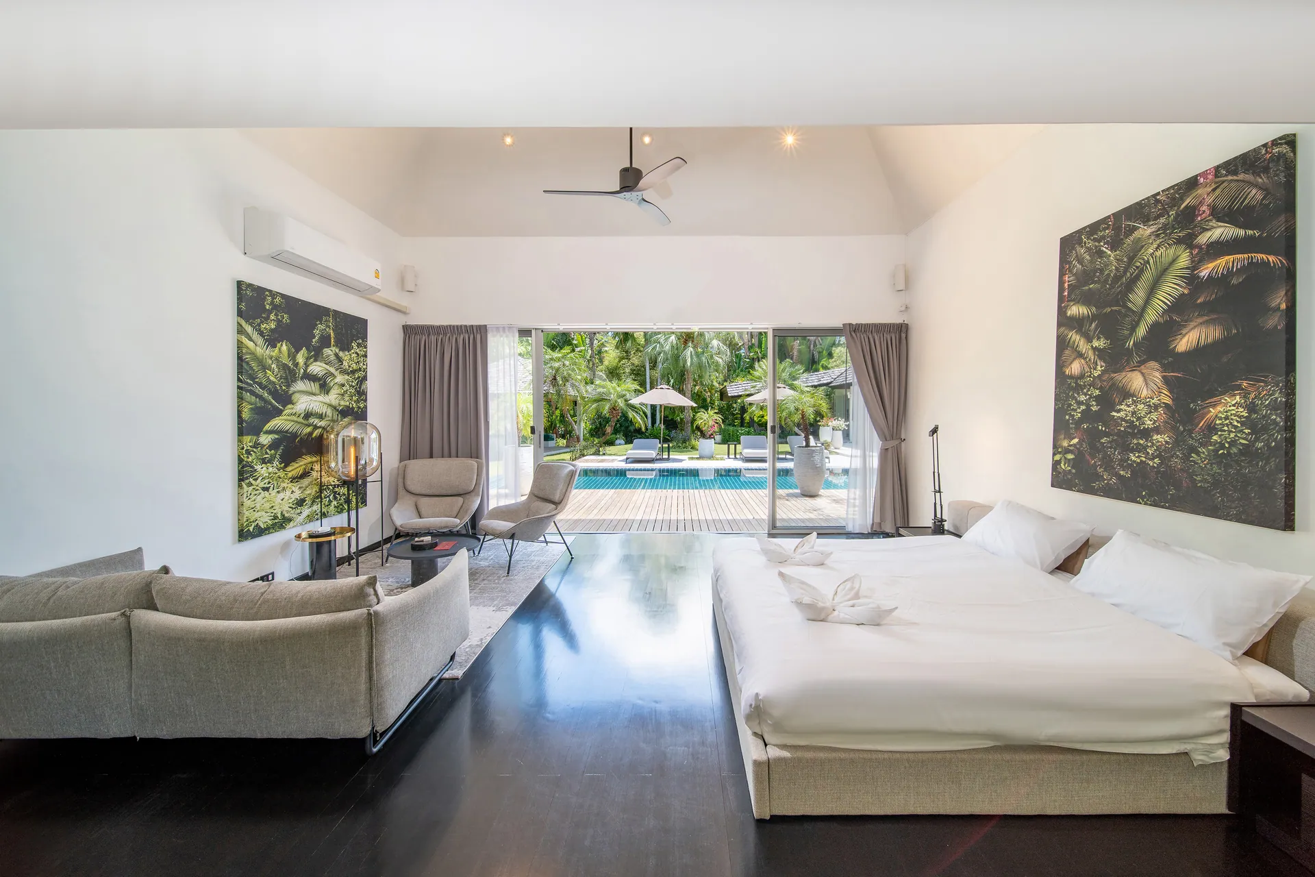 Bedroom with a large bed, a sofa and lounge chairs, opening through glass doors onto the pool deck