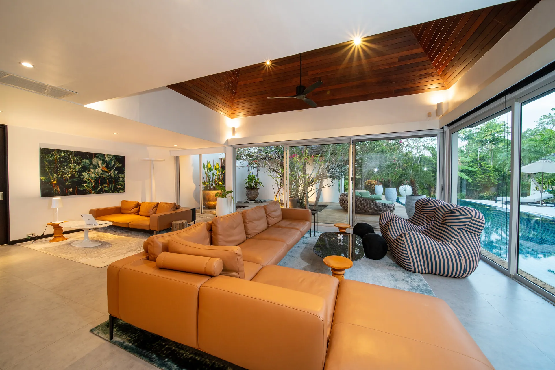 Living room under a timber-lined ceiling, with a leather sectional sofa and glass walls opening to the pool