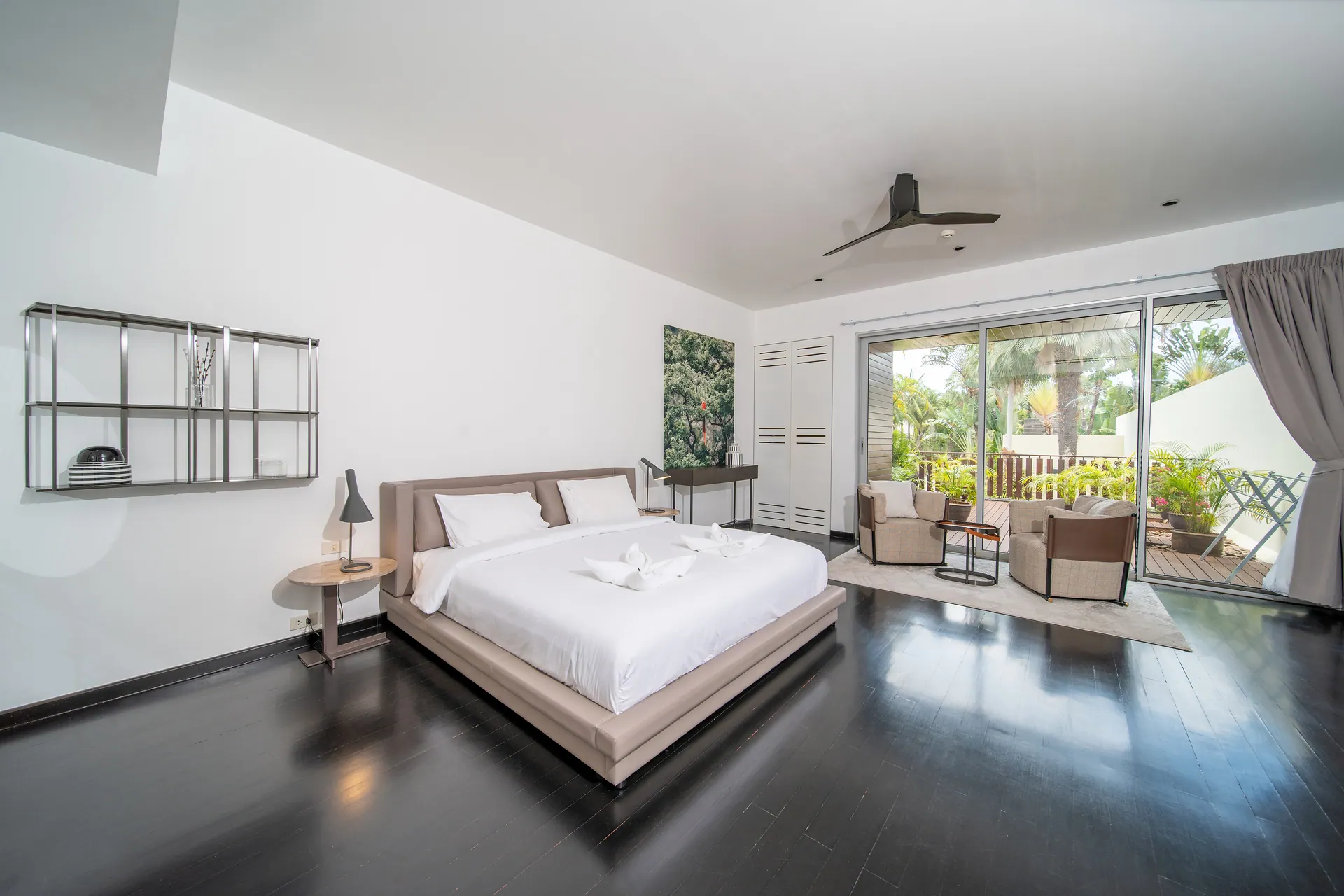 Bedroom with an upholstered bed, two armchairs by the window and glass doors to a planted terrace