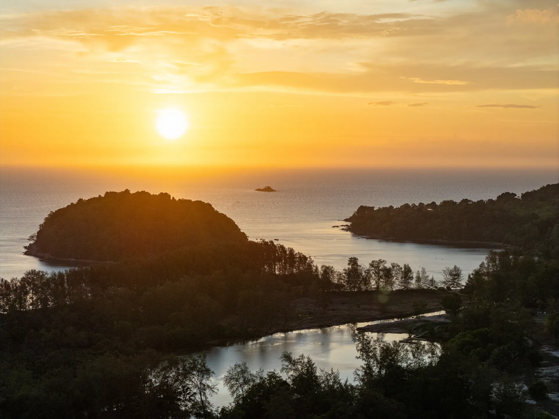 Drone view at sunset over a wooded headland, a lagoon and a small island offshore