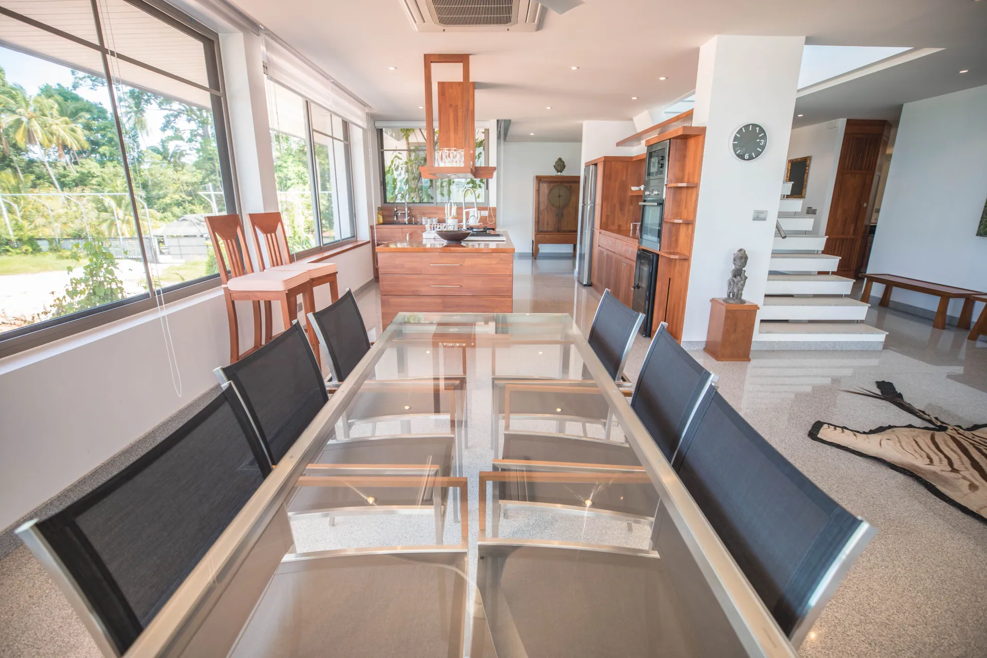 Long glass dining table leading to the open kitchen and a staircase