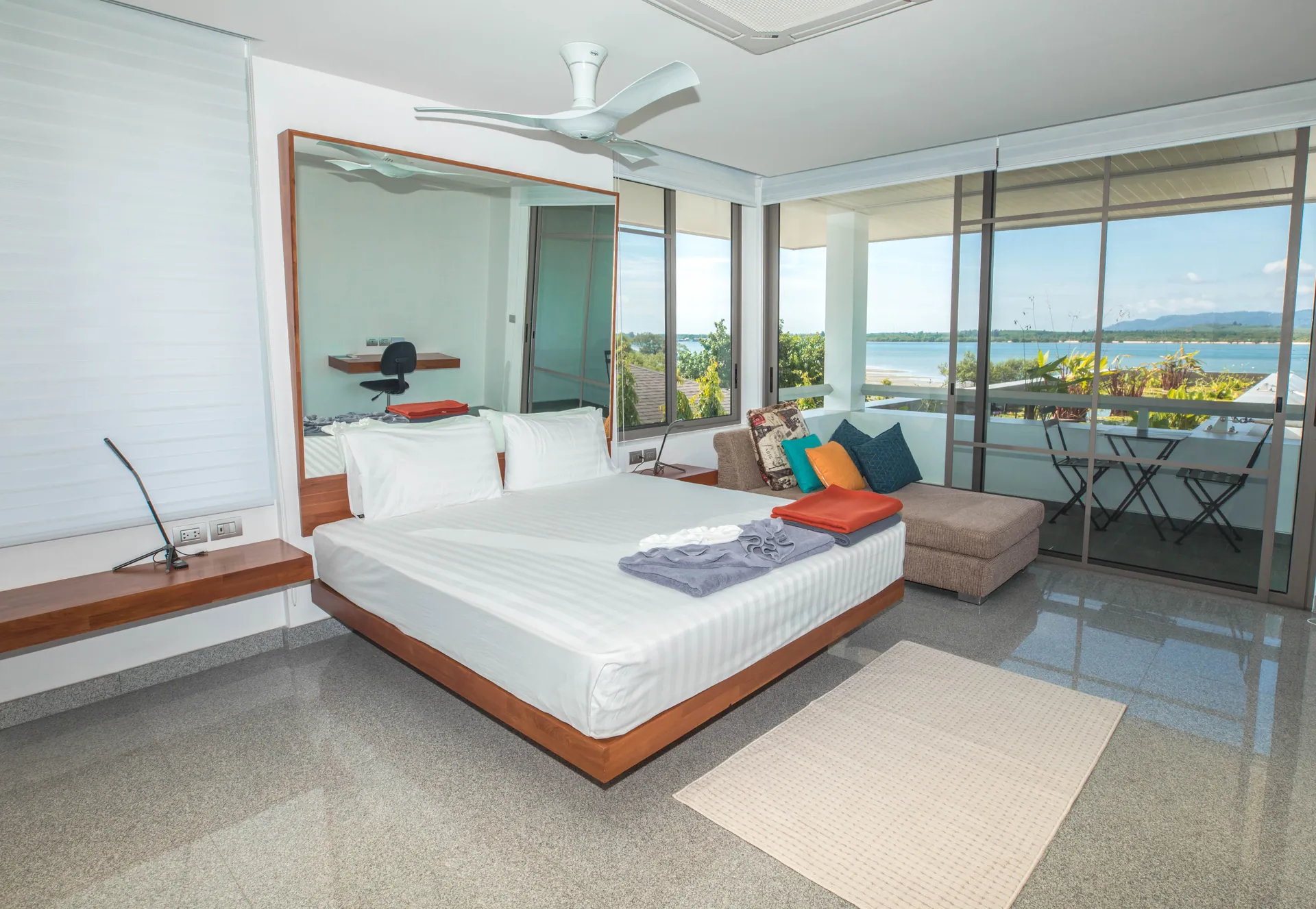 Bedroom with a platform bed, a sofa and floor-to-ceiling glass opening onto a balcony over the bay