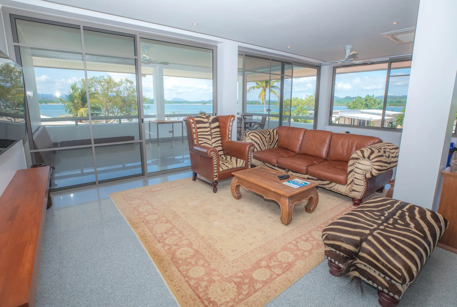 Living room with leather sofas, a teak coffee table and sliding glass doors facing the bay