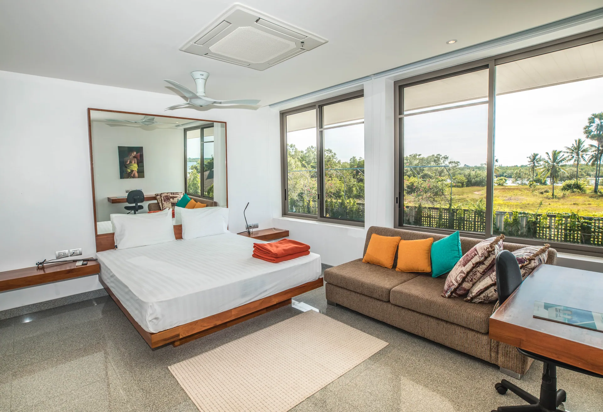 Bedroom with a platform bed, a sofa with orange cushions and wide corner windows onto the countryside