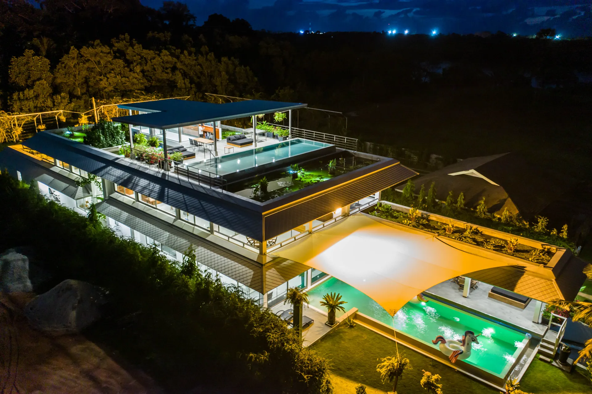 The villa at night from above, with the rooftop pool, the lily ponds and the garden pool lit