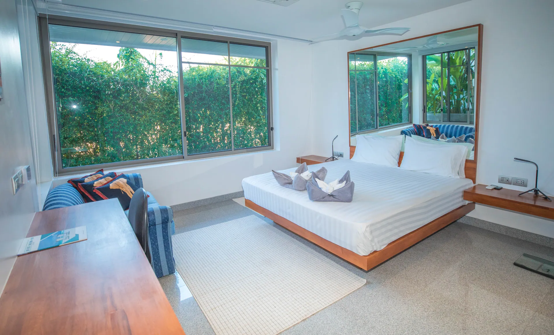 Bedroom with a platform bed, a striped blue sofa and a desk, with windows onto the garden