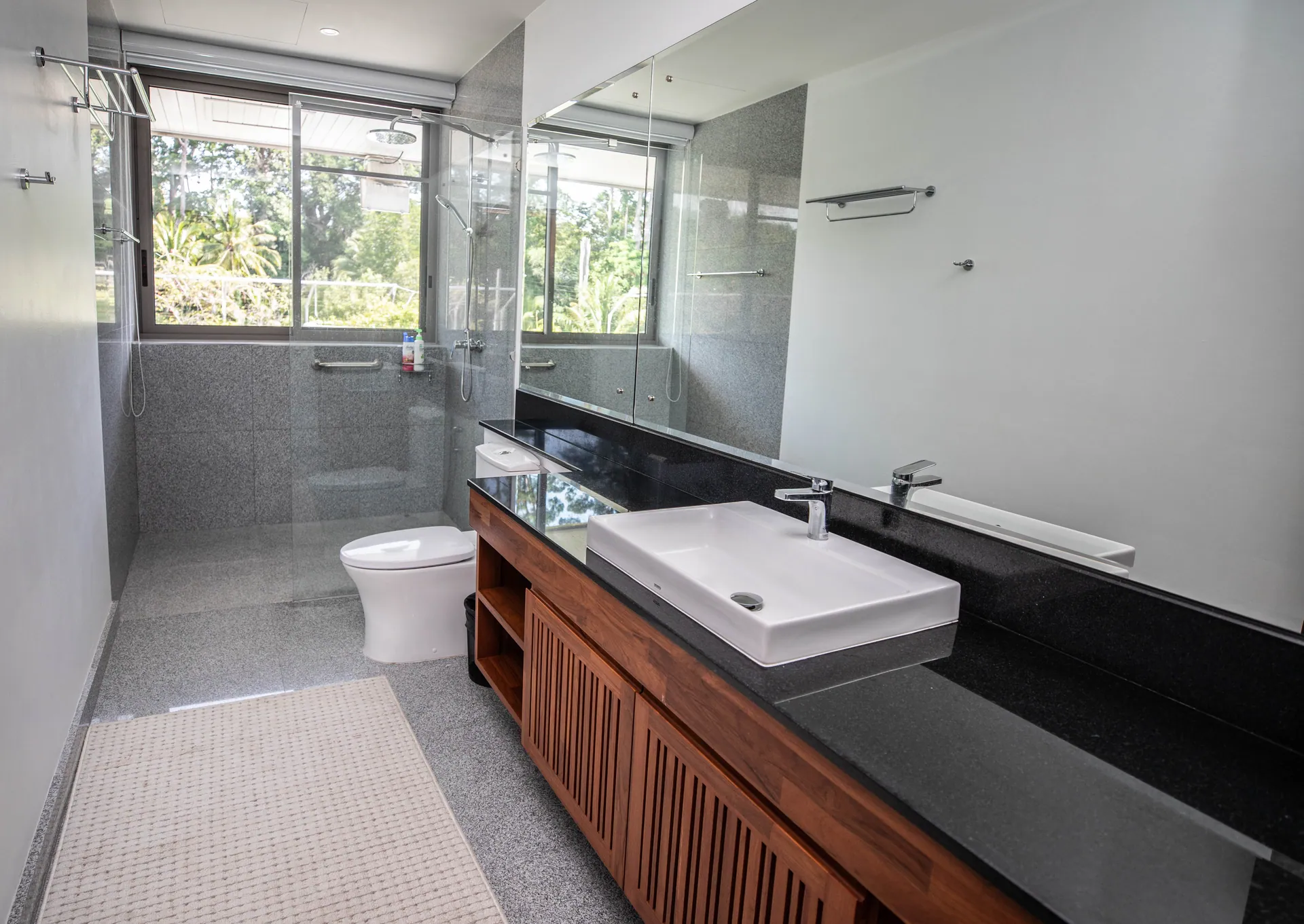 Bathroom with a vessel basin on a black stone counter, a teak vanity and a glass-screened shower