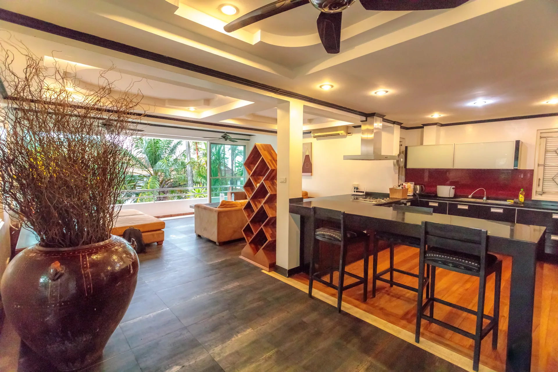Open kitchen with a breakfast bar and high stools, windows onto the greenery behind