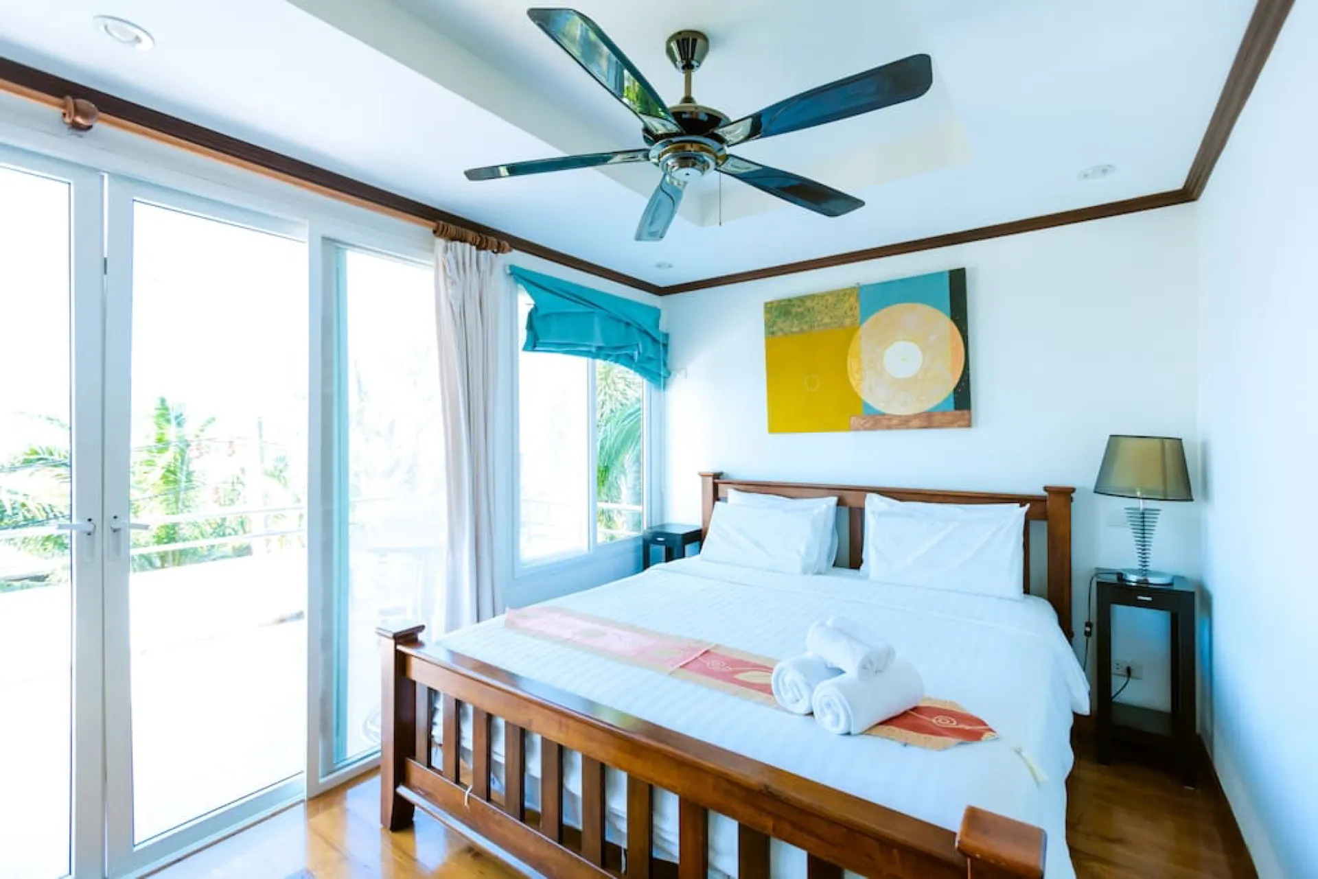 Bedroom with a timber bed, bright artwork, a ceiling fan and glass doors to a balcony