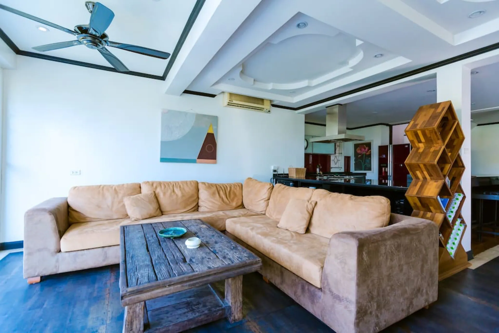 Living room with a large sectional sofa and a rustic timber coffee table, the kitchen beyond