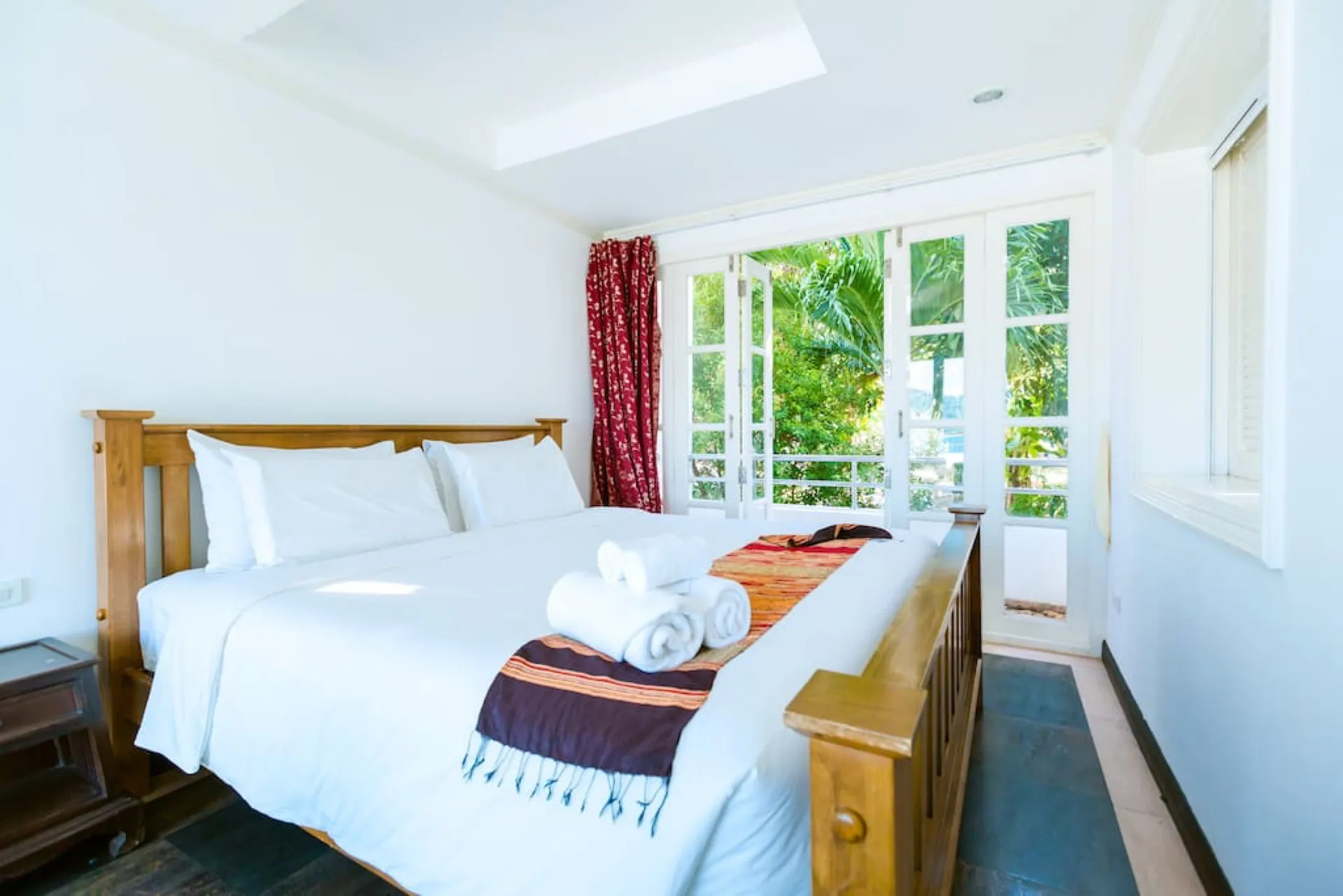 Bedroom with a timber bed, red curtains and French windows to the garden