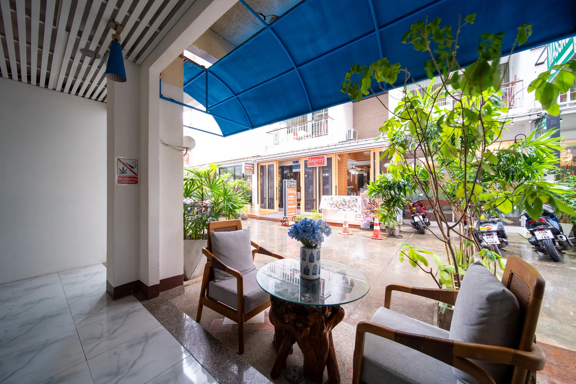 Armchairs and a glass table under a blue awning at the hotel entrance