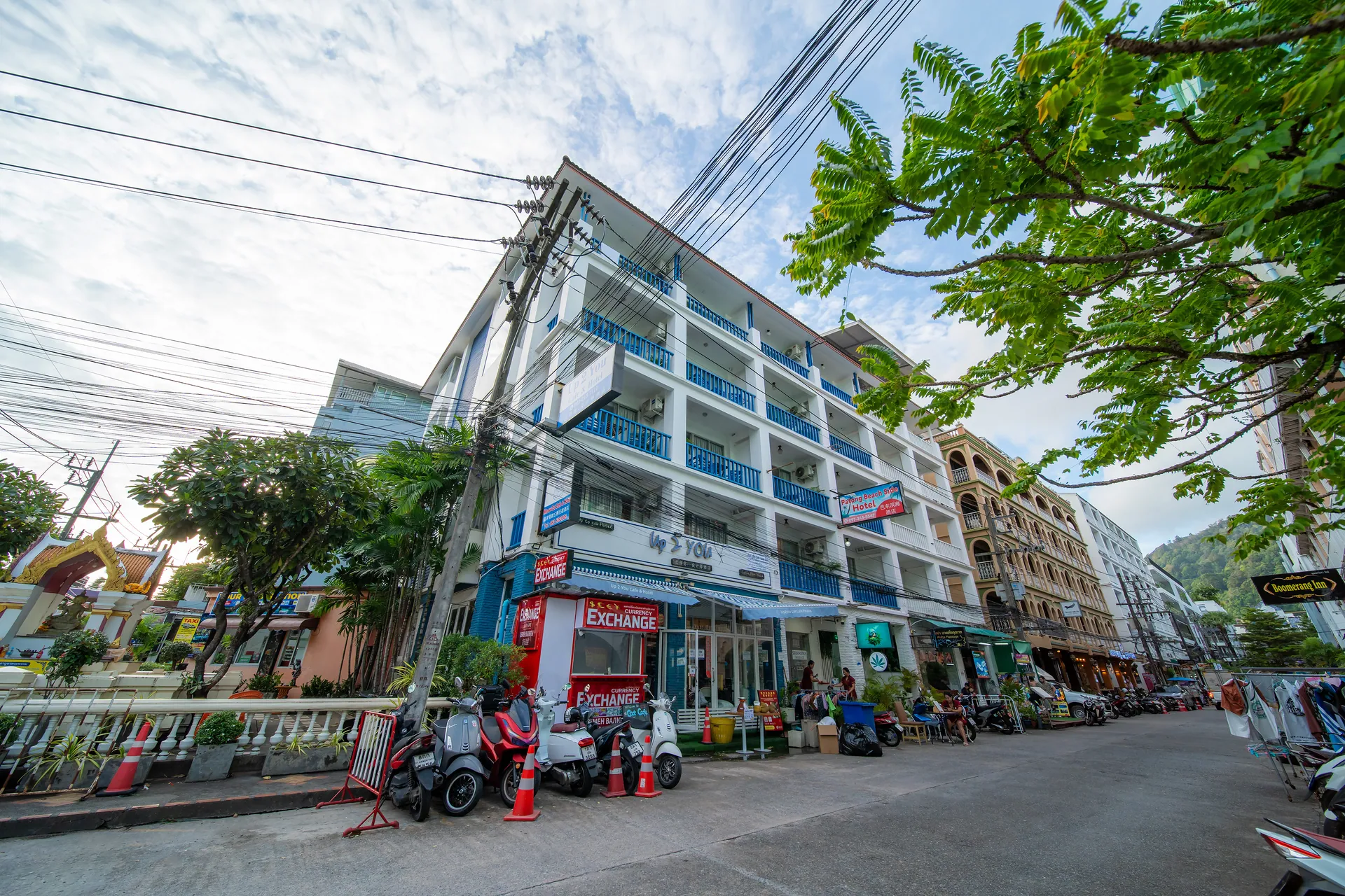 The hotel building on a Patong street, with blue balcony railings above ground-floor shops